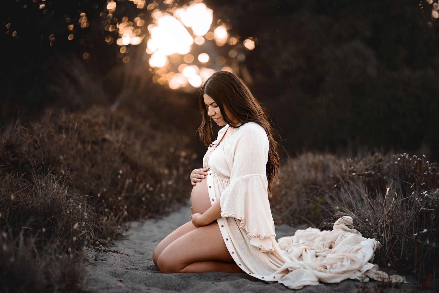 Maternity photo of woman in white dress at sunset in a field.