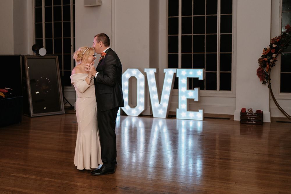 Dancing couple with illuminated LOVE sign during wedding reception.
