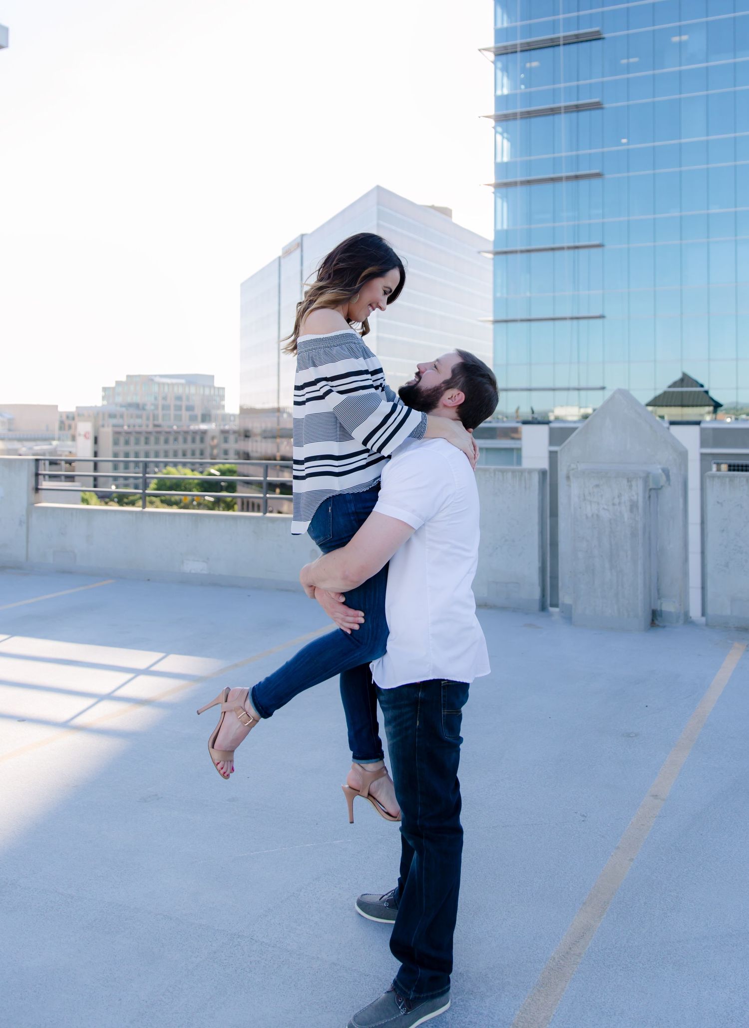 Marco holding Tonya up while they look at each other smiling on the top of a parking garage in downtown Boise Idaho.