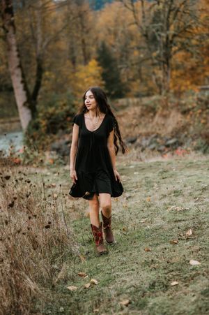 Figure in a black dress walks along a hillside trail surrounded by golden autumn foliage.