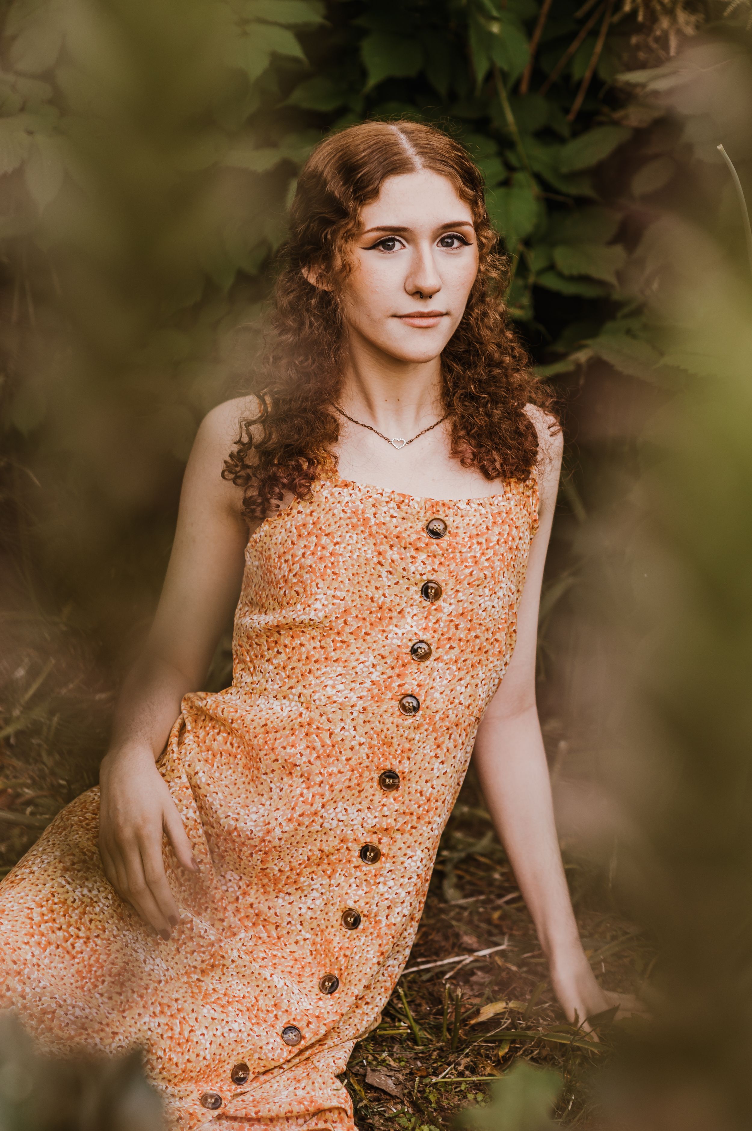 Vintage-inspired portrait in peach floral buttoned dress amid natural foliage.