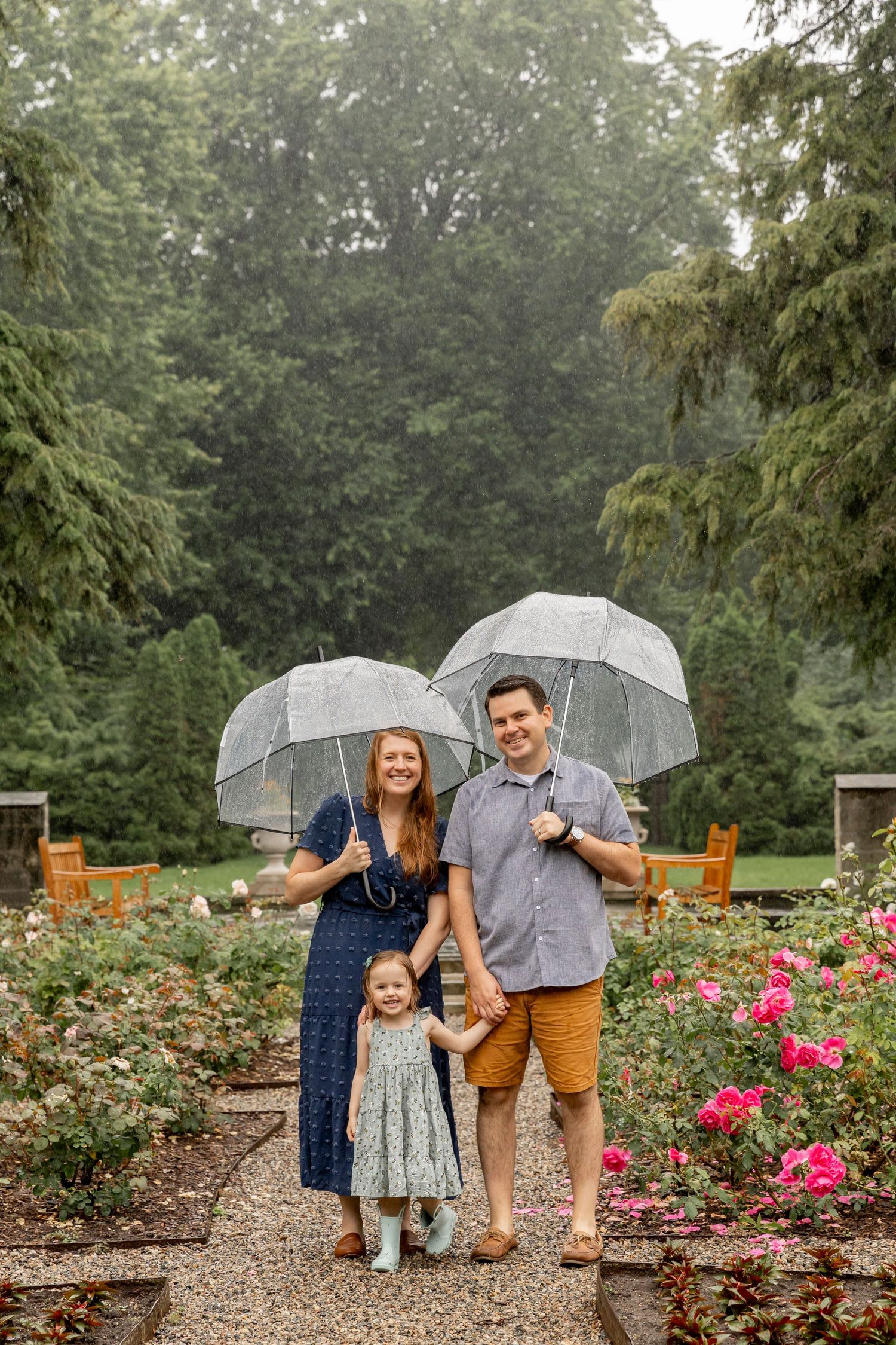 family of three holding clear umbrellas and smiling in the rain for a family photo at Henry ford