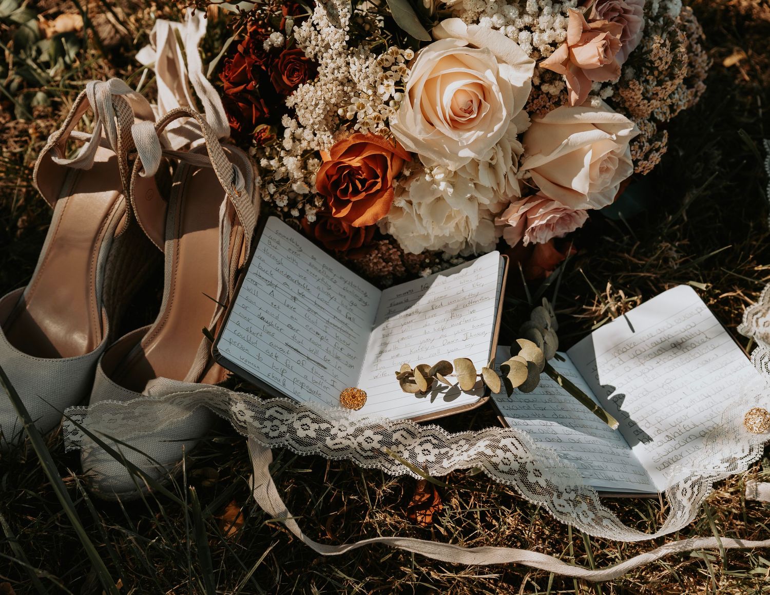 Wedding flatlay with beige heels, handwritten notes and pink roses on textured surface.