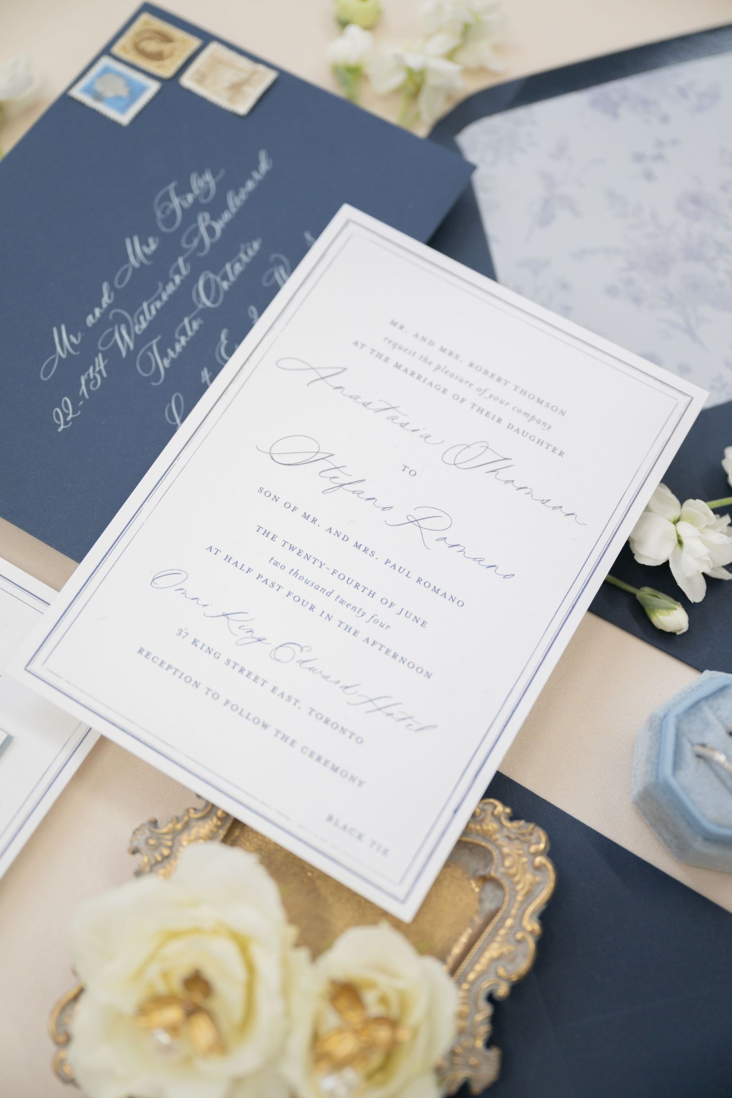 Wedding invitation suite featuring navy envelopes and elegant calligraphy with white floral accents.