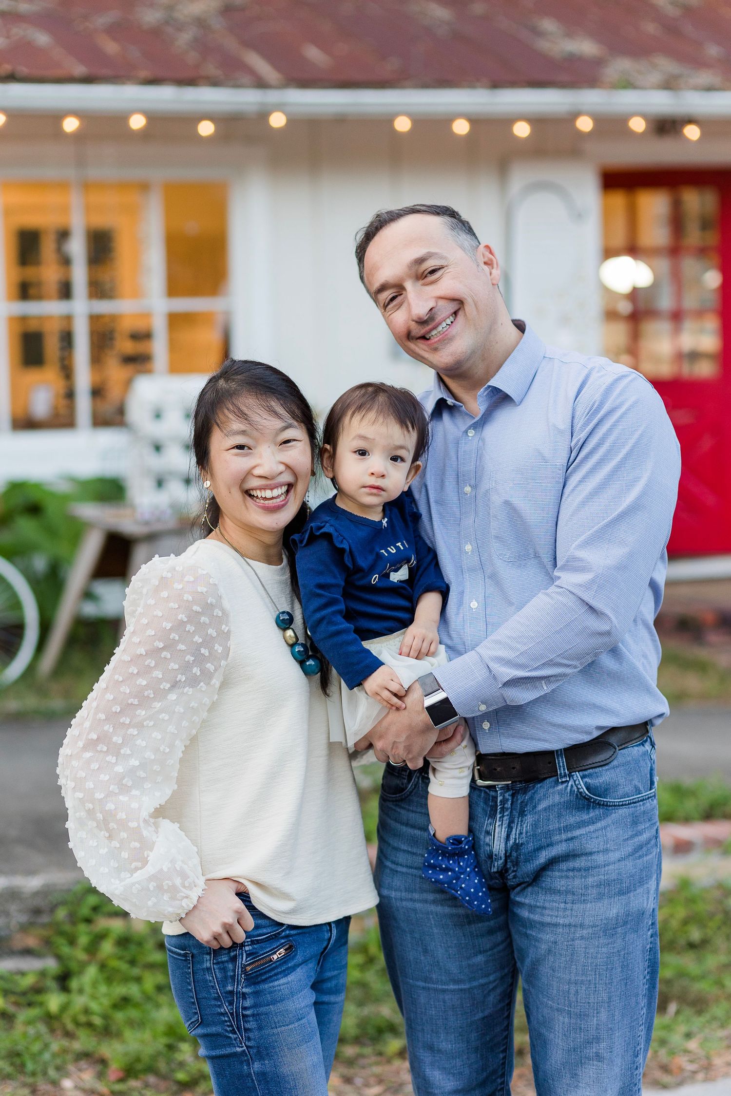 A family wearing coordinated blue and white outfits poses together in front of a building with string lights.