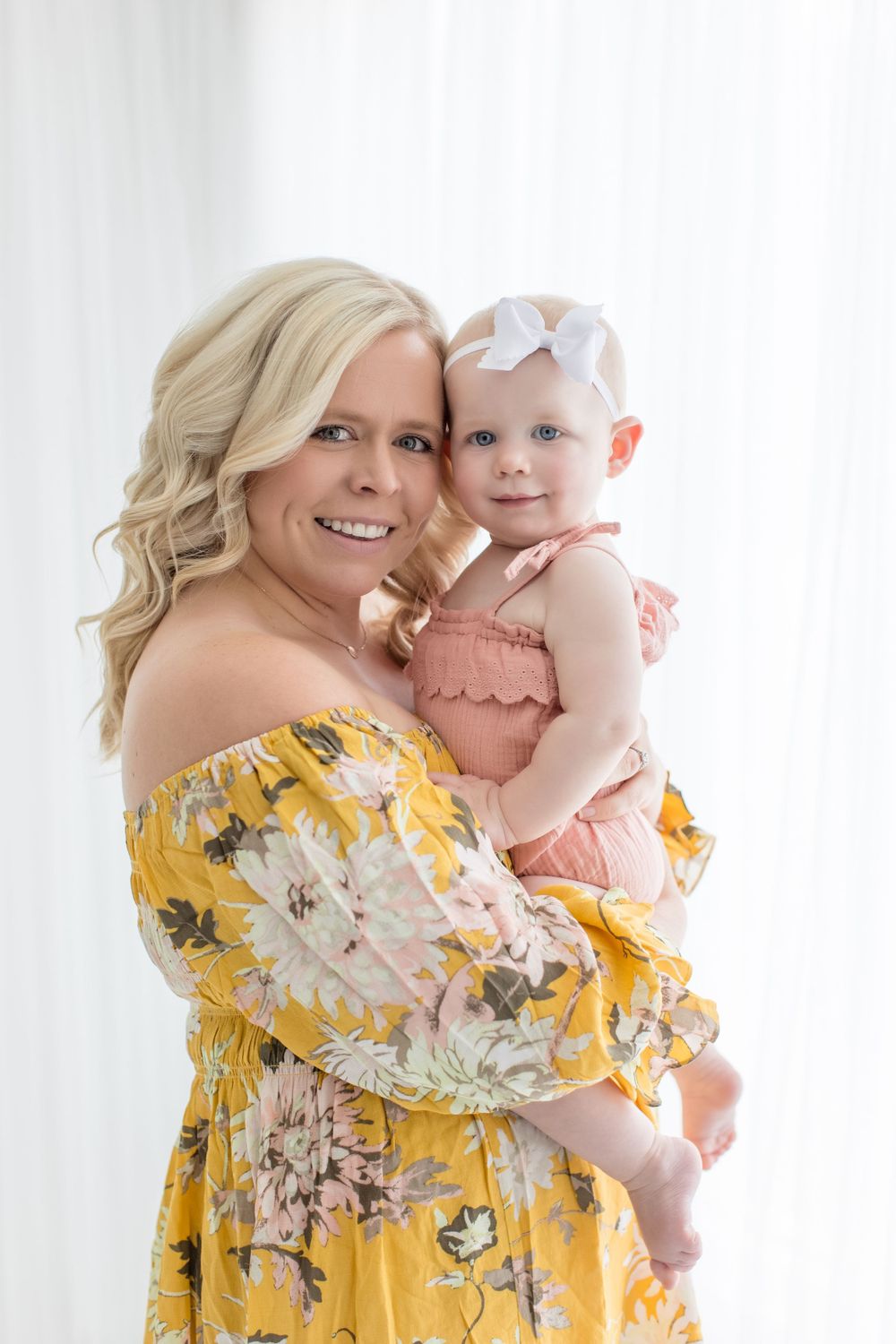 A tender moment captured as parent and child pose in floral yellow and pink outfits against a light background.