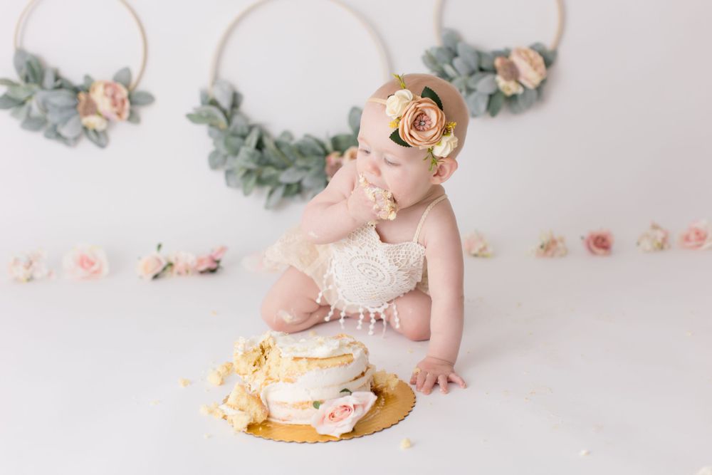 Baby enjoying cake smash photography session with vintage decor and floral accents.
