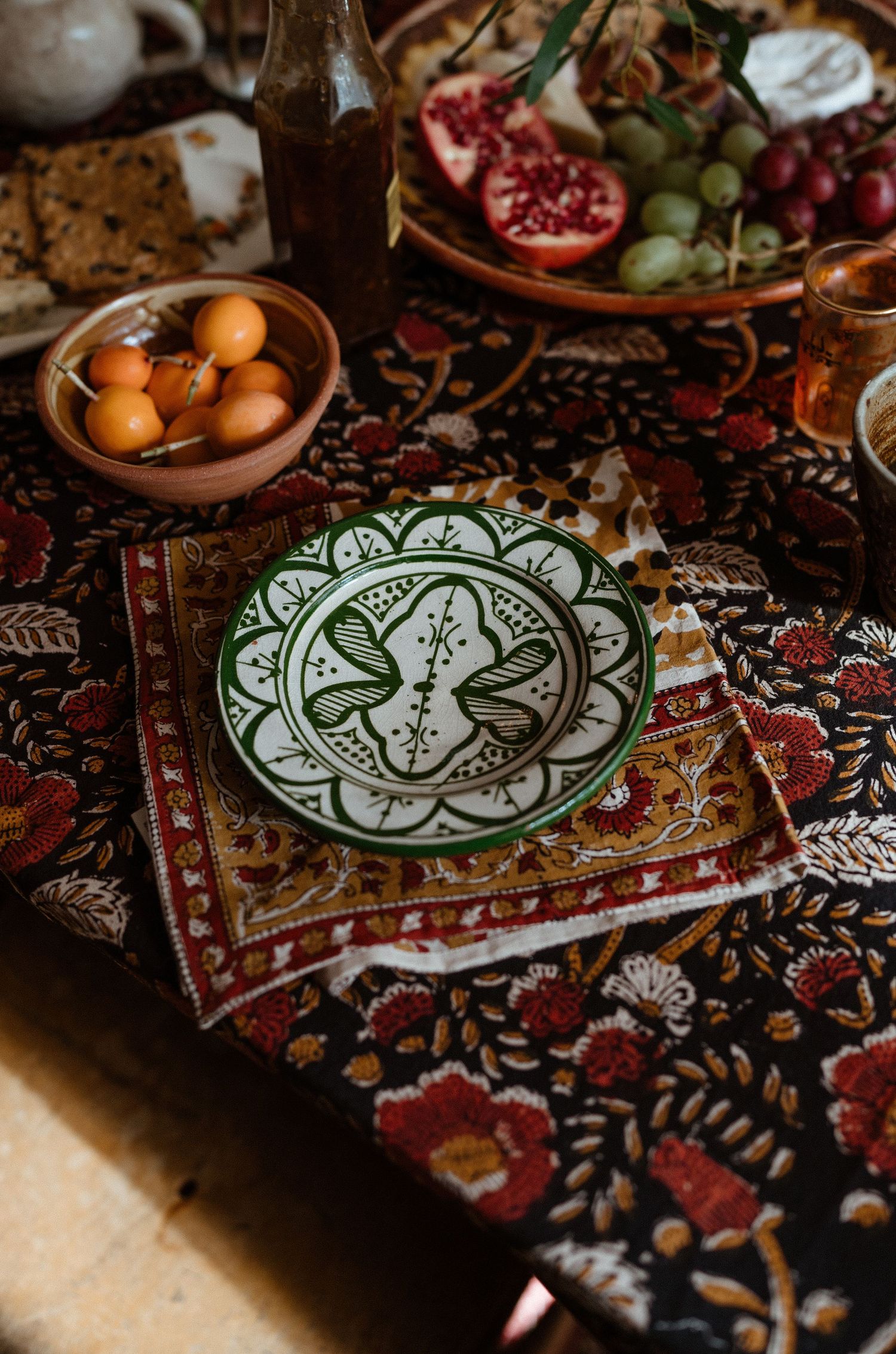 Ornate table setting with Moroccan plate, pomegranates and citrus on patterned tablecloth.