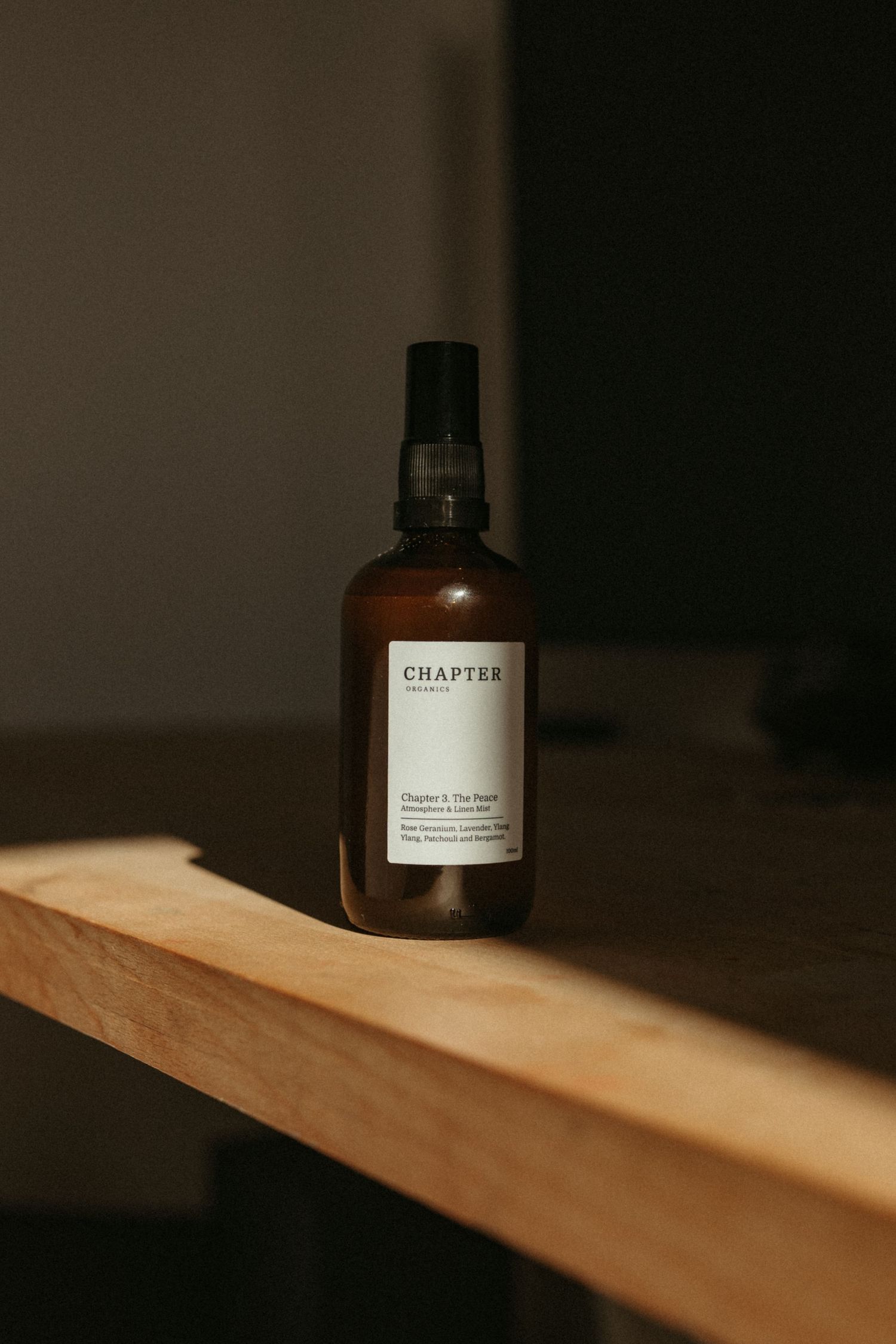A brown glass bottle with Chapter label sits on a wooden shelf in dramatic lighting.