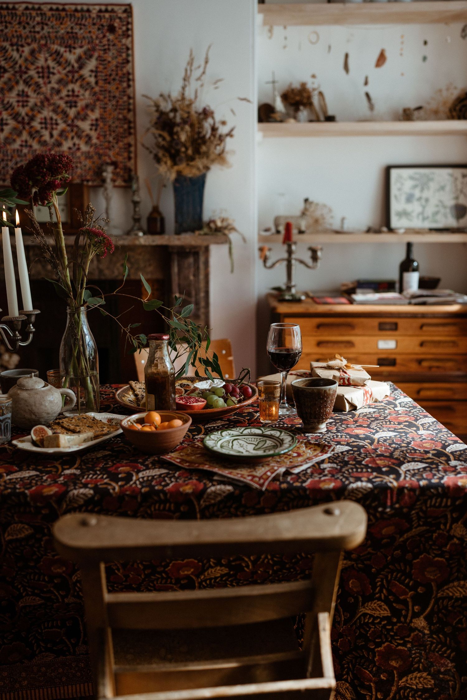 Rustic dining table set with dried flowers, candles and vintage decor against white walls.