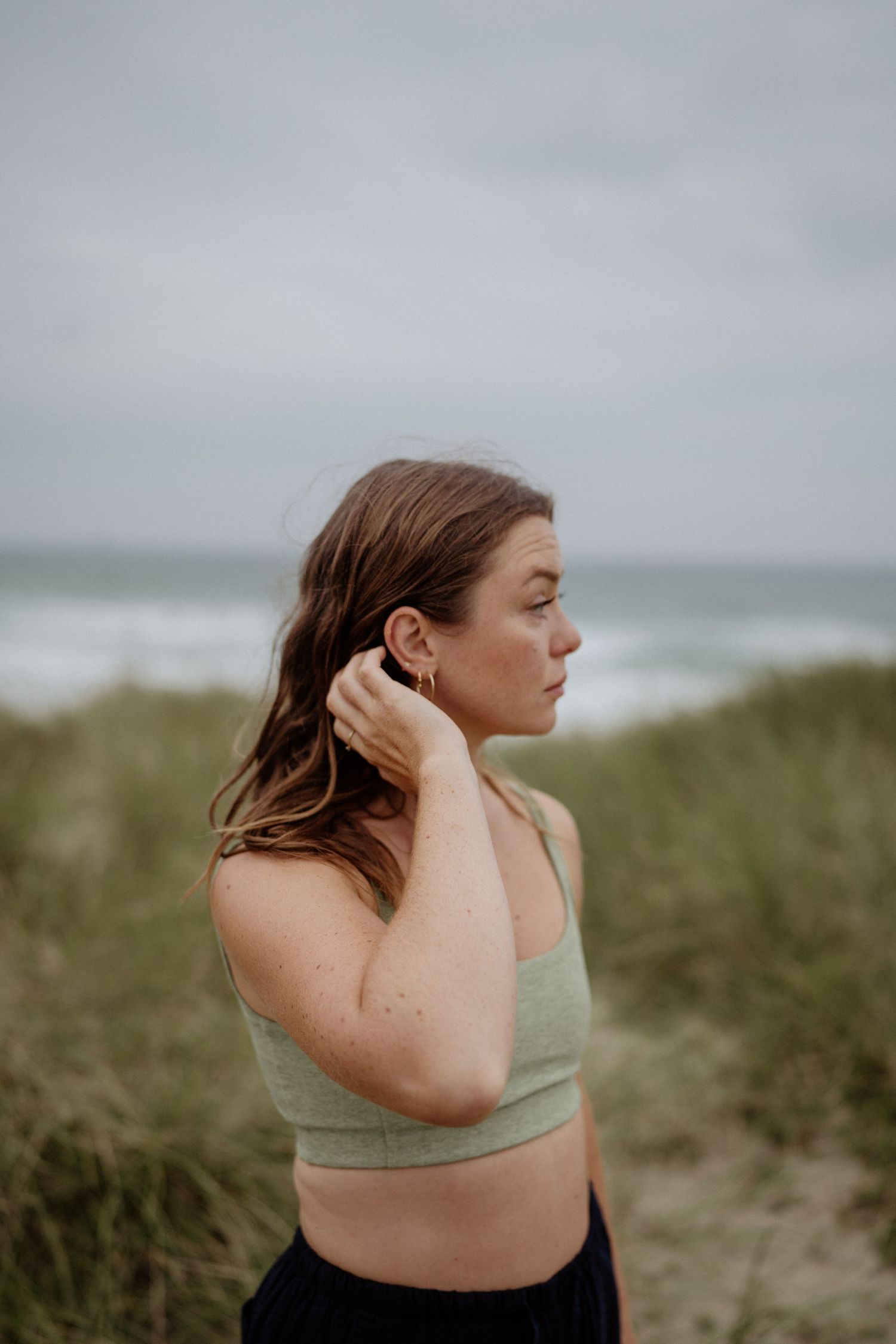 Moody coastal portrait in sage green crop top against stormy ocean backdrop.
