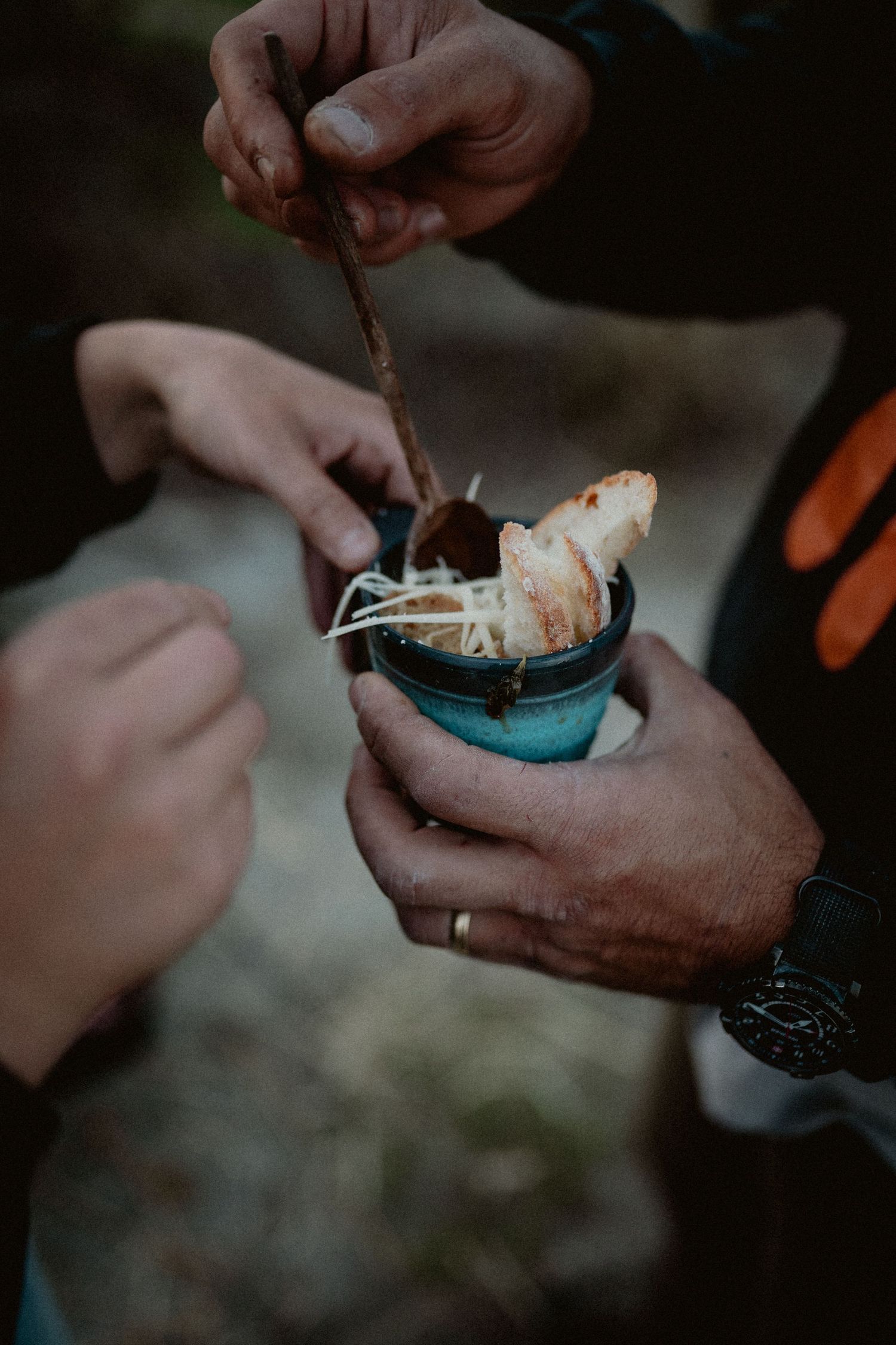 Hands holding and dipping into a small jar of food outdoors.
