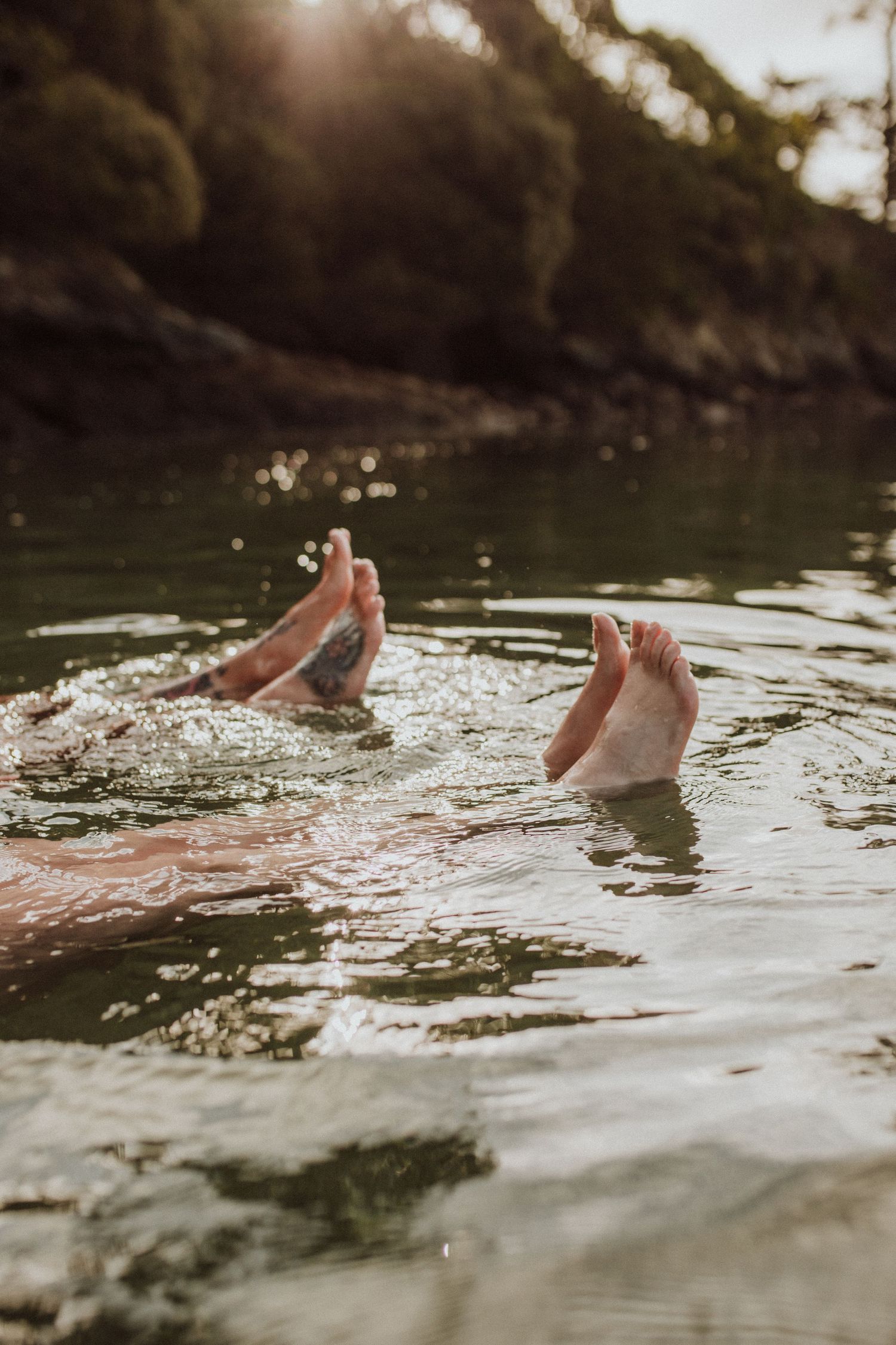 Feet playfully sticking out of water during sunset at a lake.
