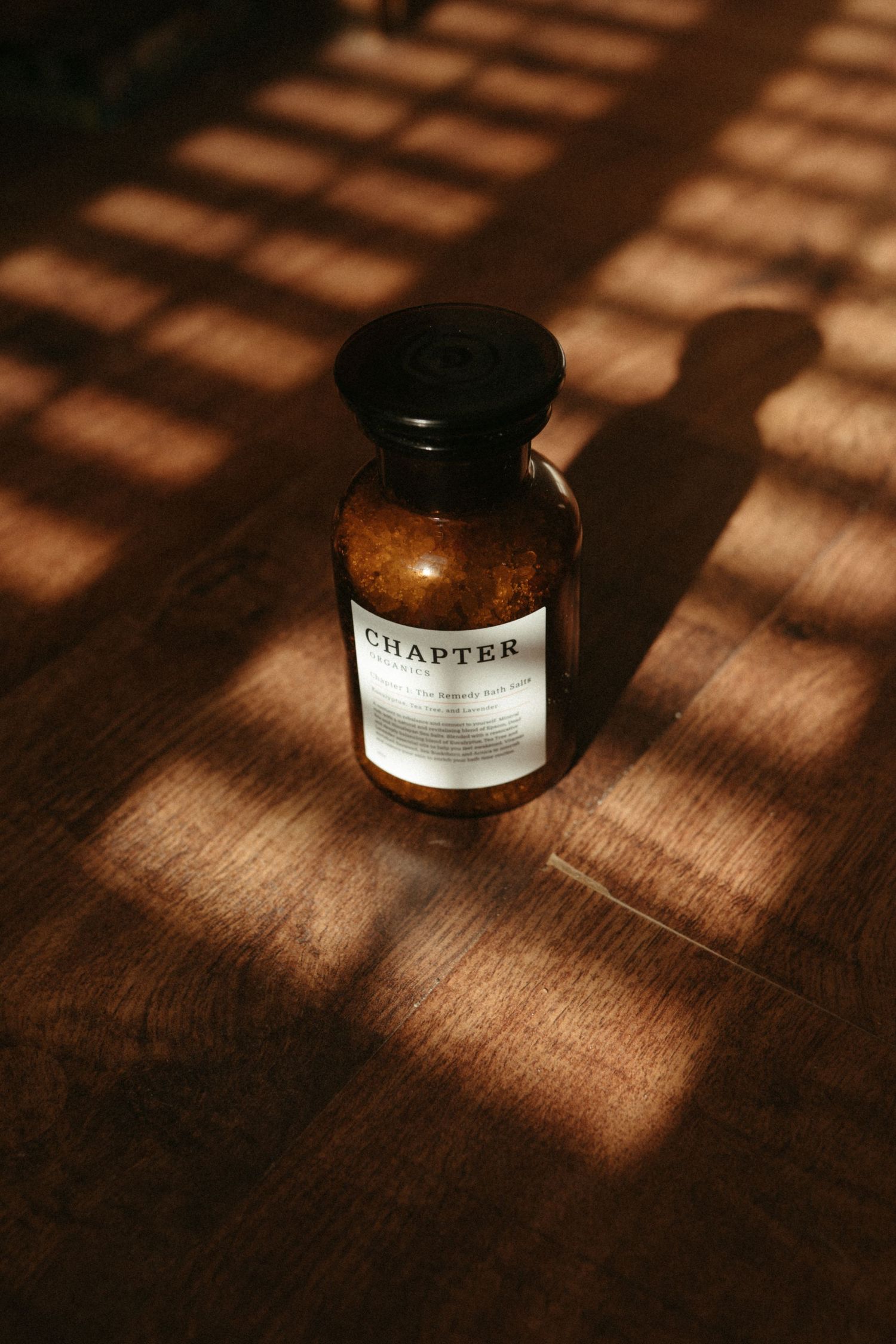 A brown glass bottle labeled Chapter casts shadows in warm sunlight on wooden surface.