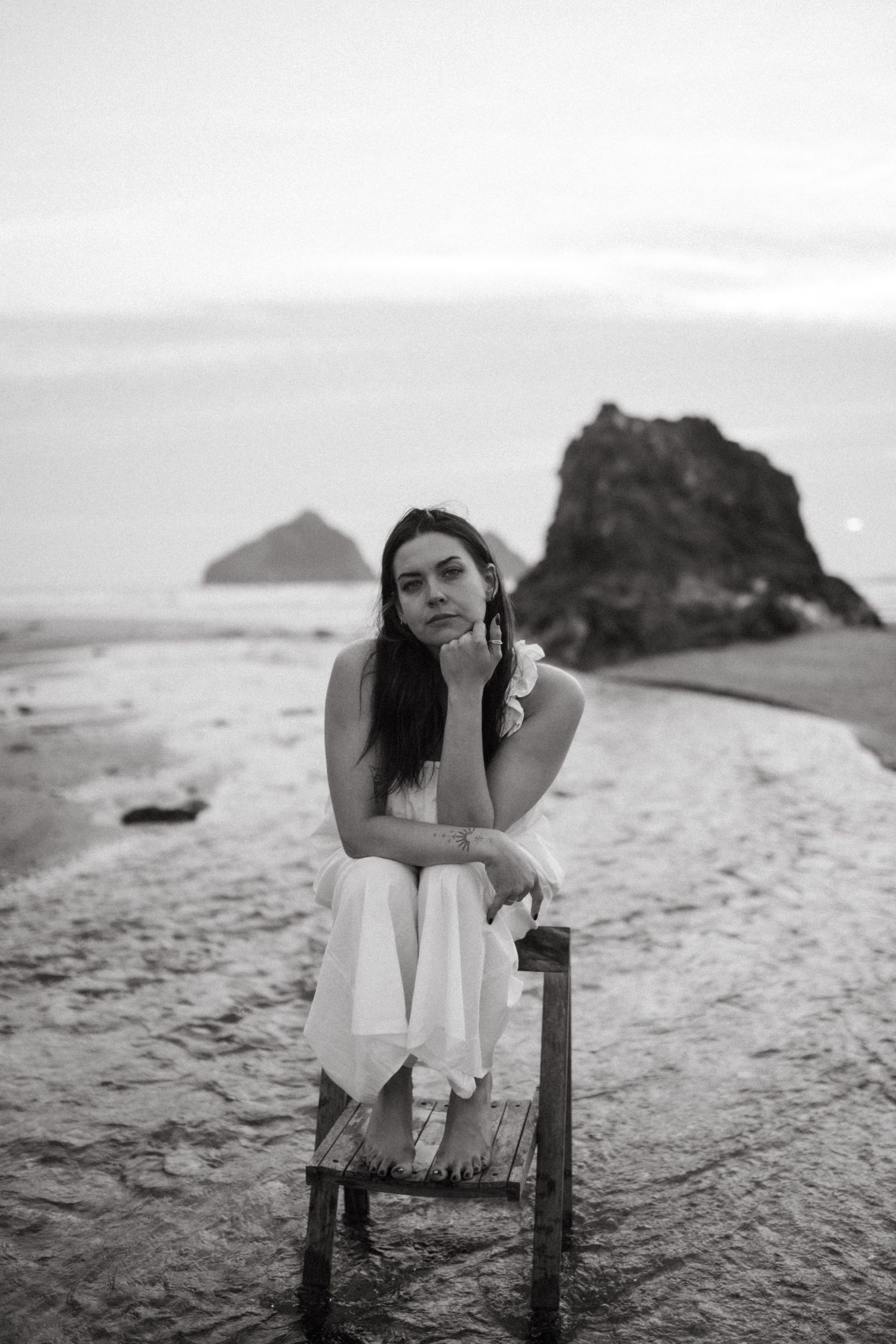 A coastal scene with dramatic rock formations forms the backdrop for an artistic portrait.