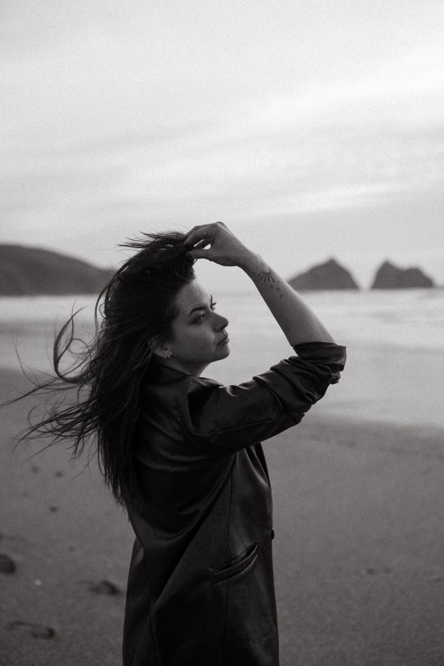 A dramatic black and white coastal portrait shows wind-swept hair against ocean rocks.