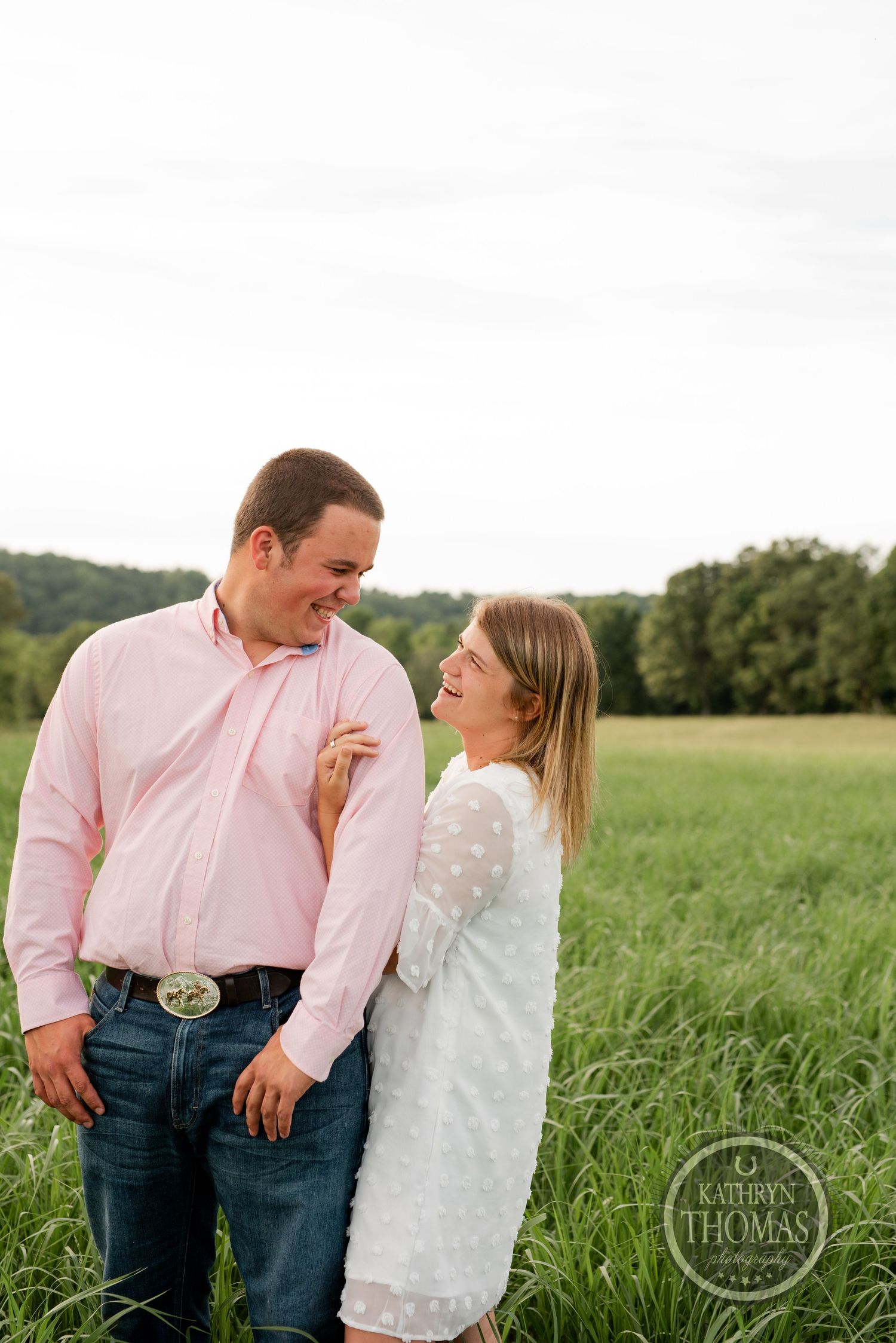 Couple sharing playful moment in grassy field wearing pink and white.
