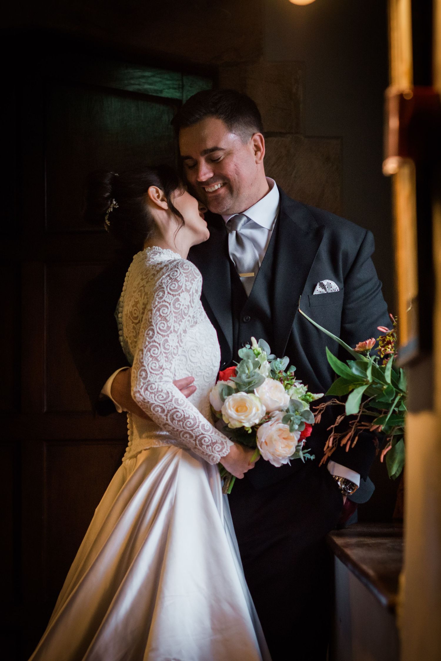 Bride and groom embrace in a dark hallway withe the light of a window the the right