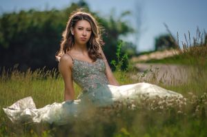 A senior teen girl sits in the grass.