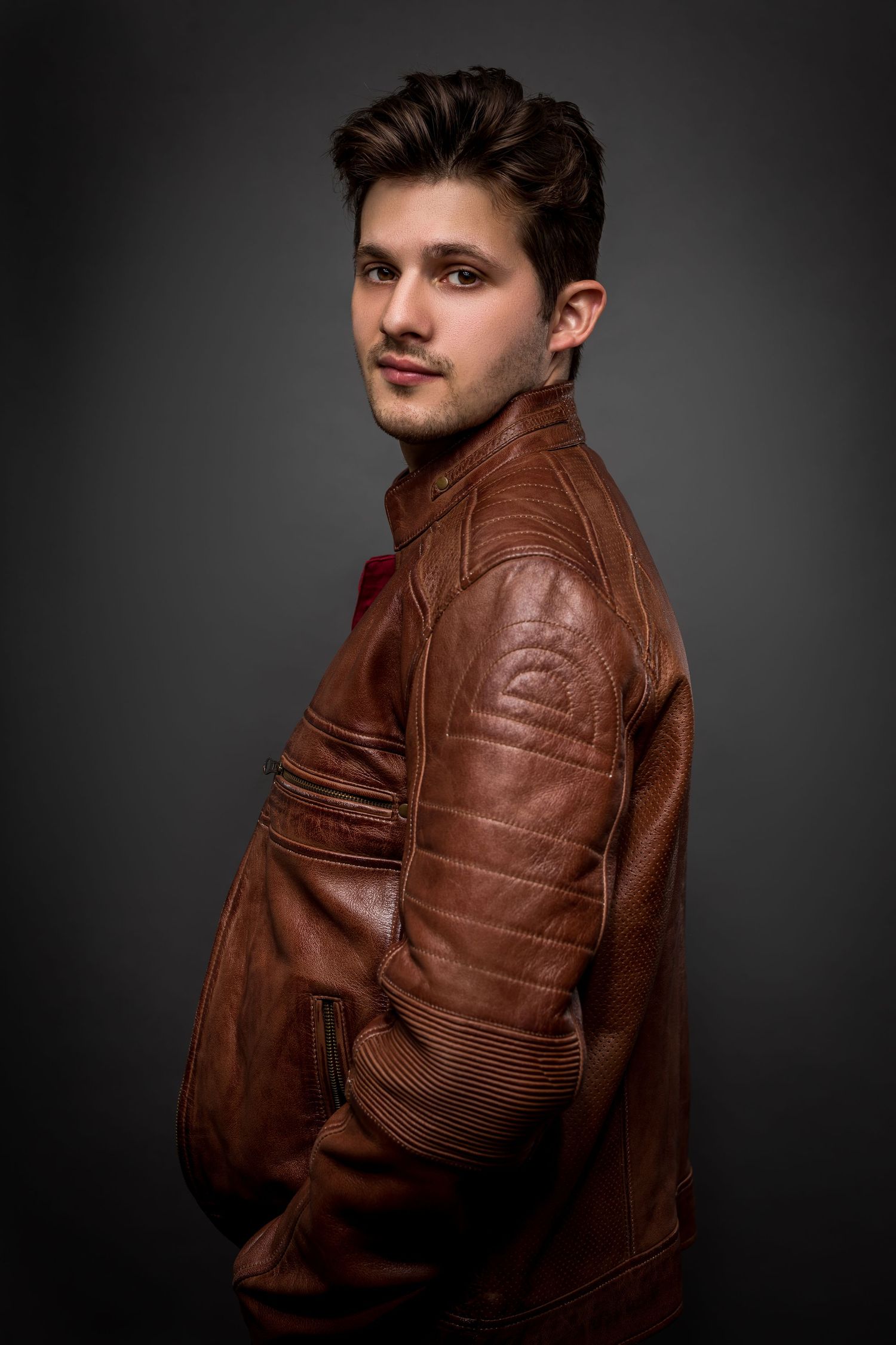 Studio fashion portrait showing brown leather jacket against dark background.