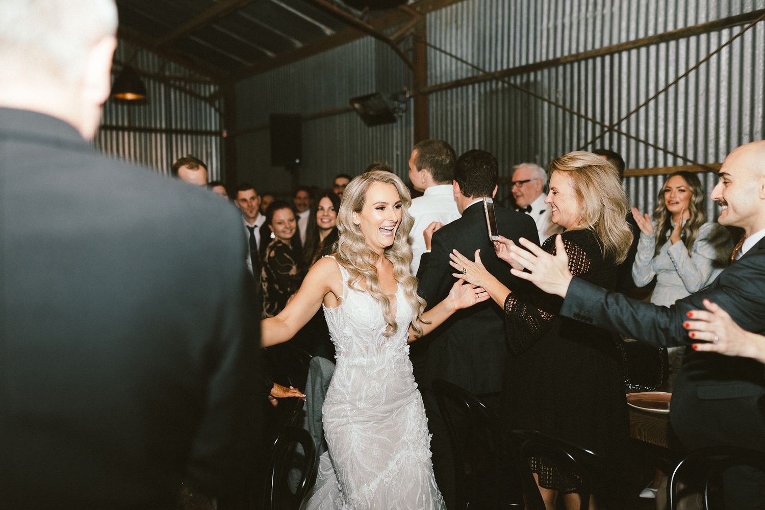 Wedding guests dance and celebrate on the dance floor at an indoor industrial-style reception venue.