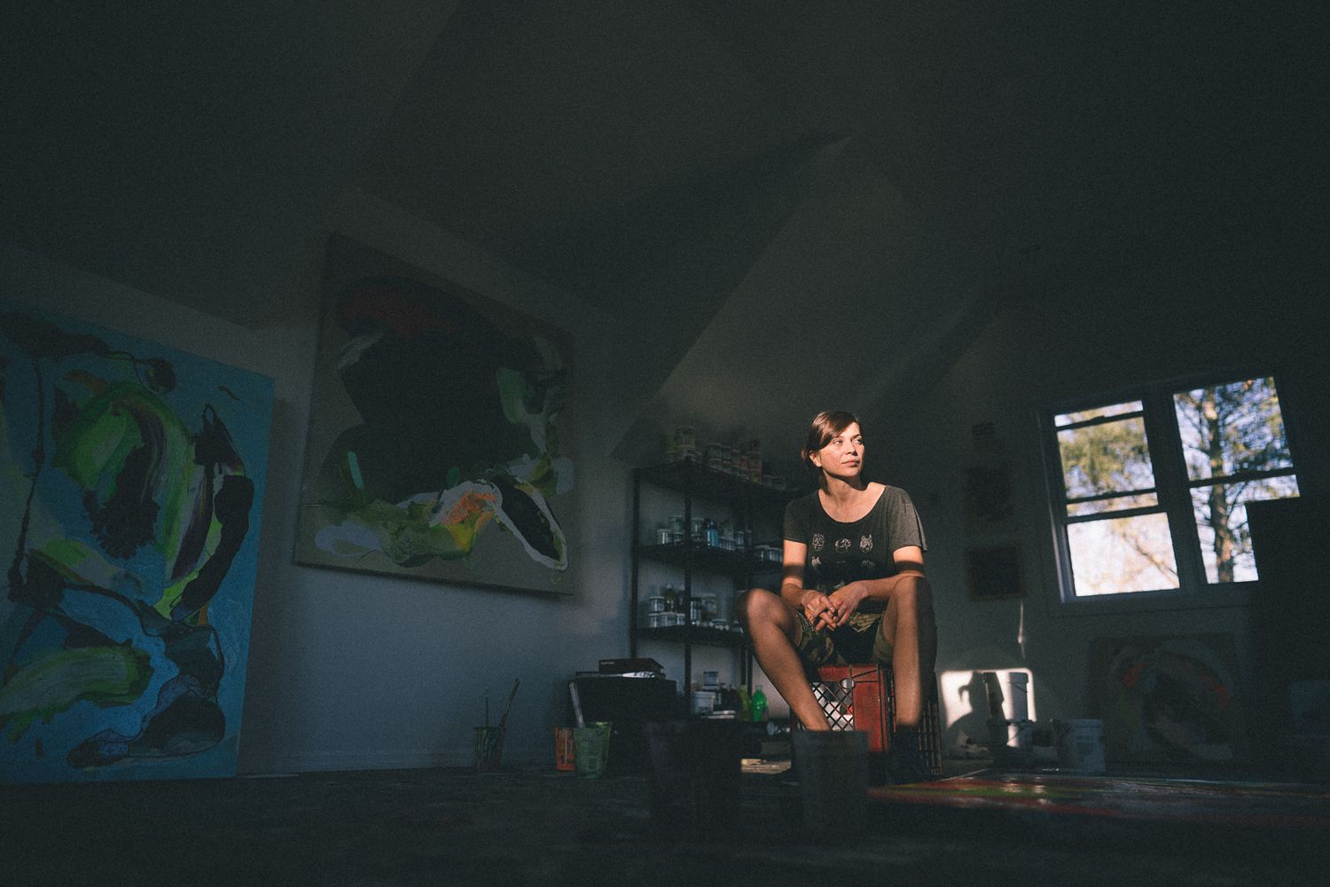 A dimly lit room with colorful wall art features someone sitting in a casual pose.
