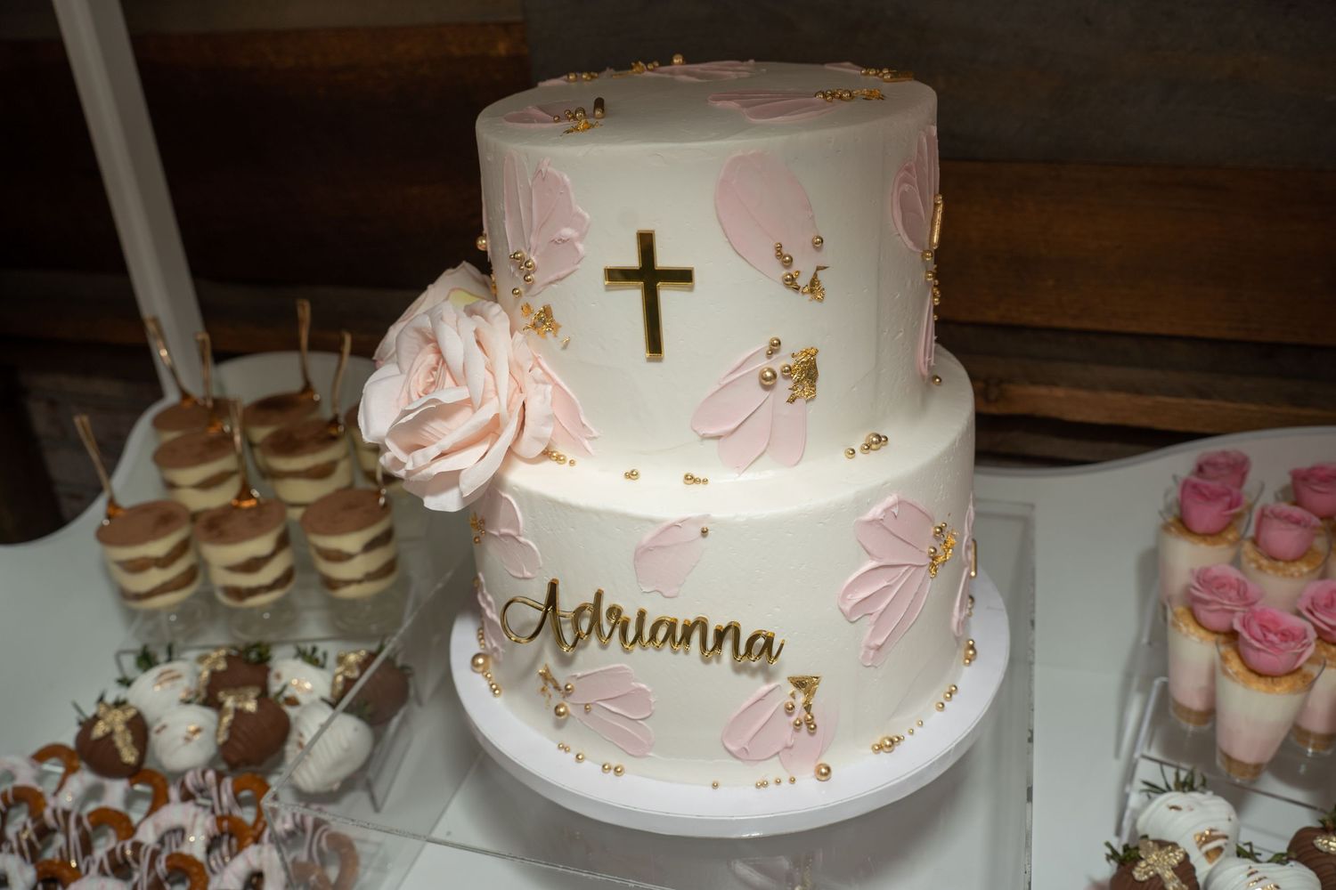 Elegant white tiered cake with delicate pink floral decorations and religious symbols.