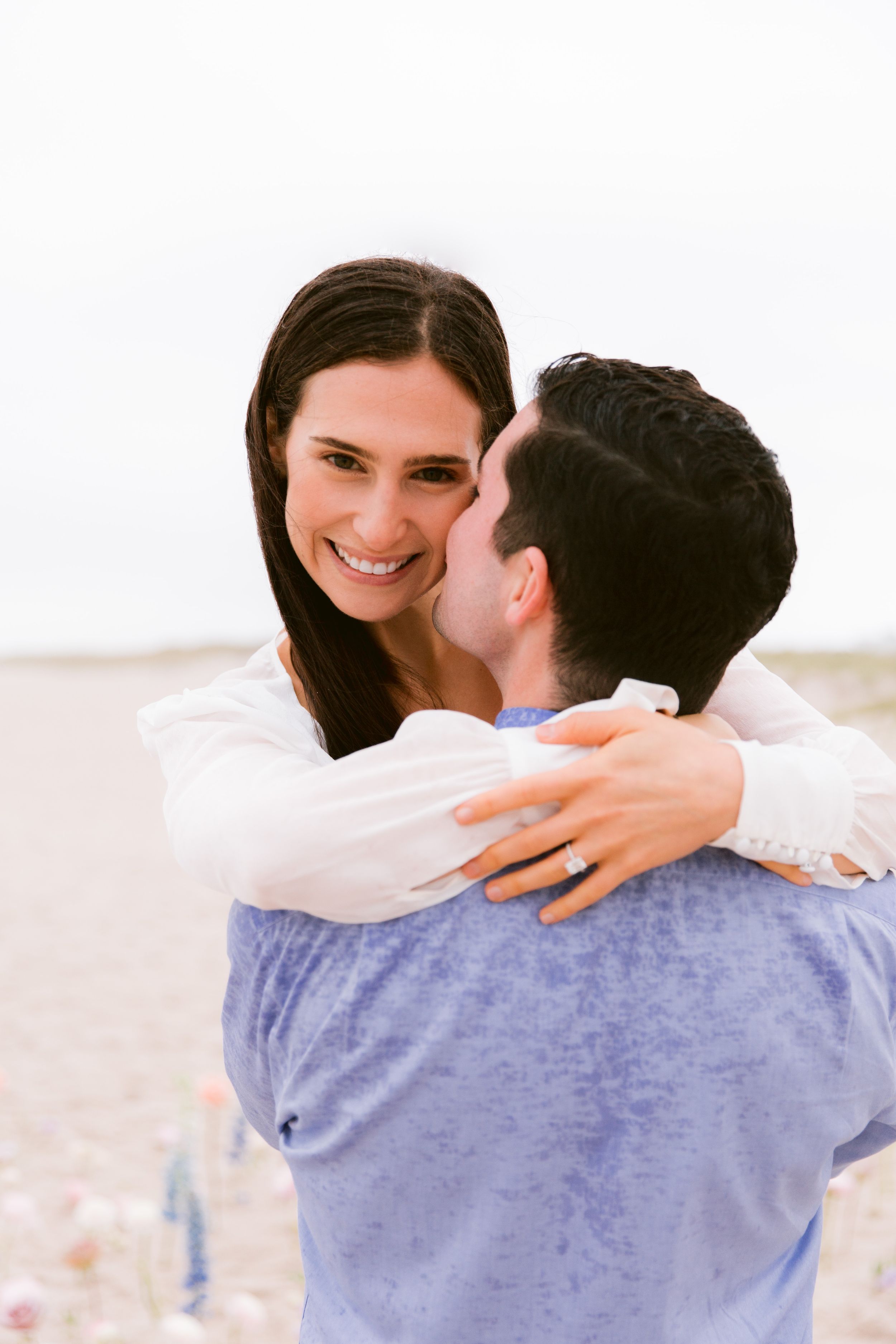 A romantic photoshoot sequence showing a joyful embrace on a beach with a light blue shirt.