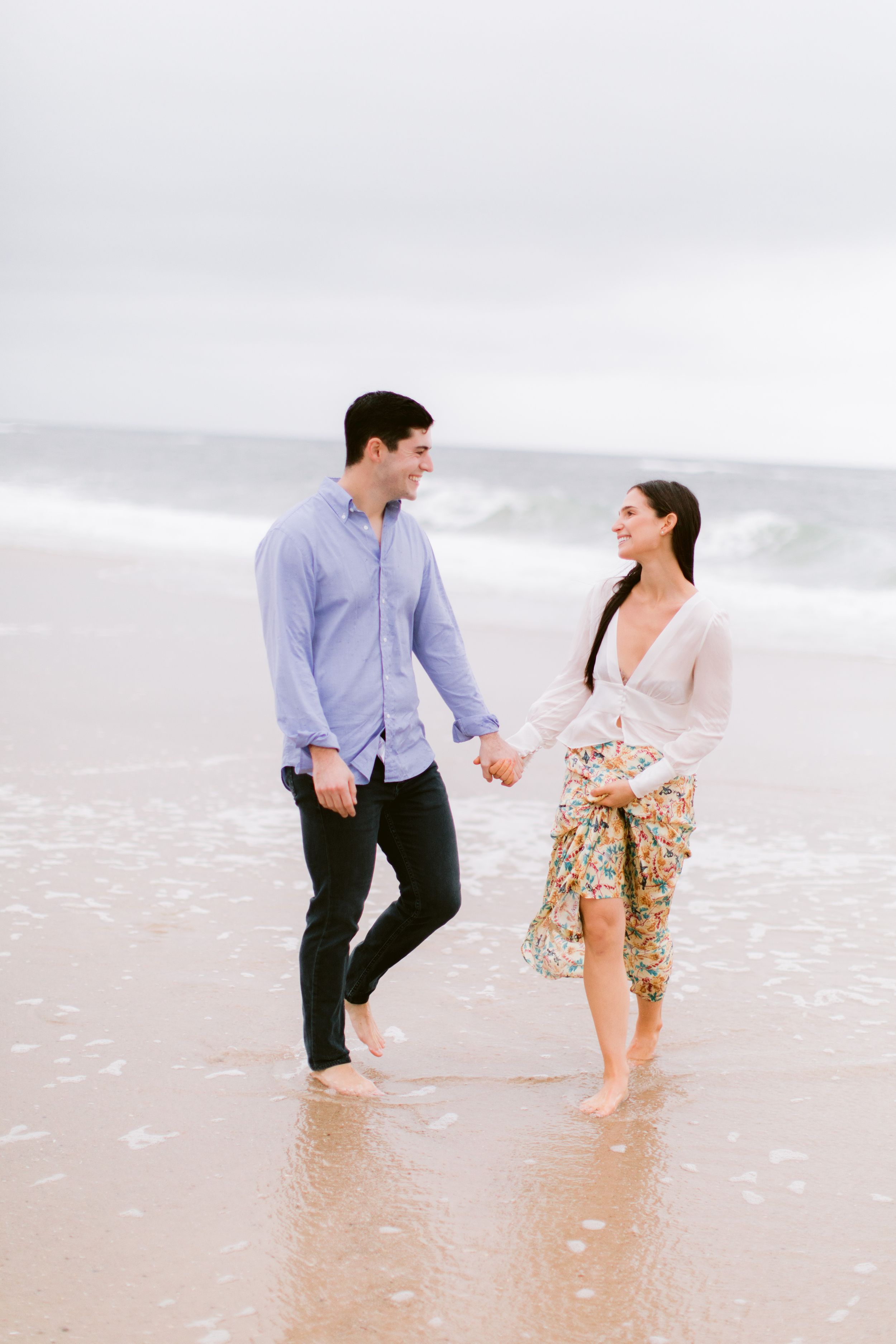 Couple walking hand in hand and playing in shallow ocean water.