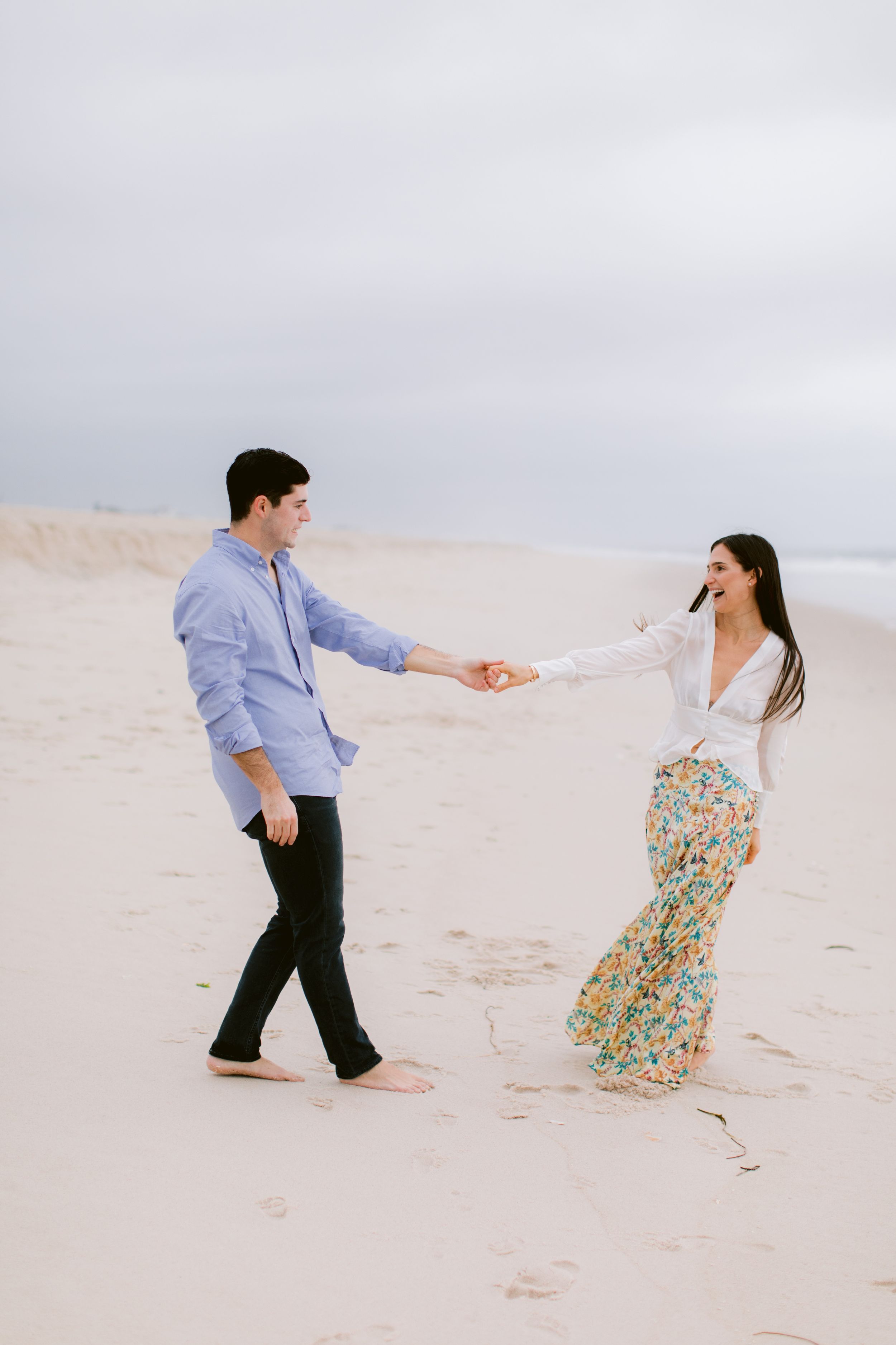 Playful couple dancing and holding hands on empty beach.