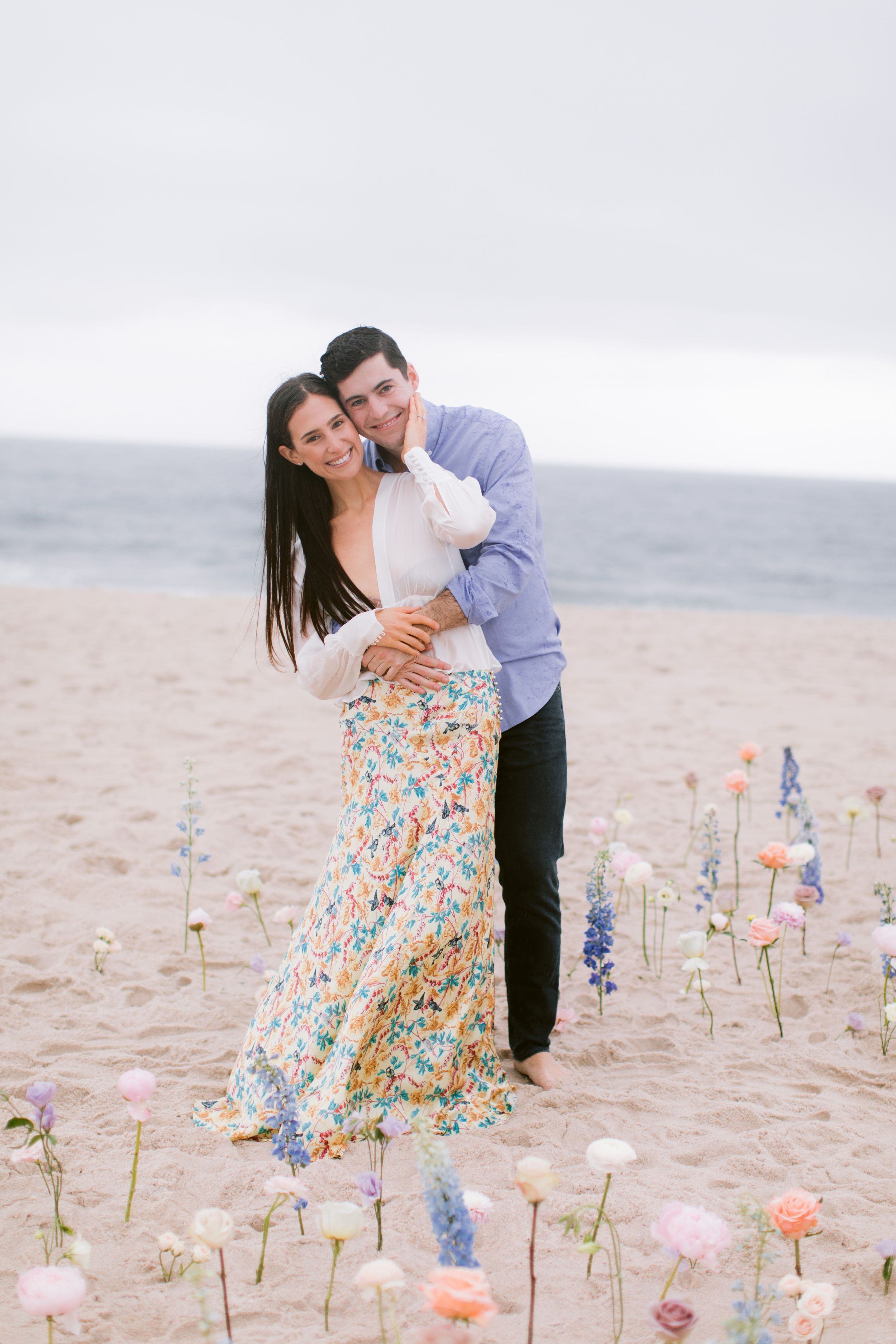 Couple embracing on beach with colorful flowers planted in the sand.