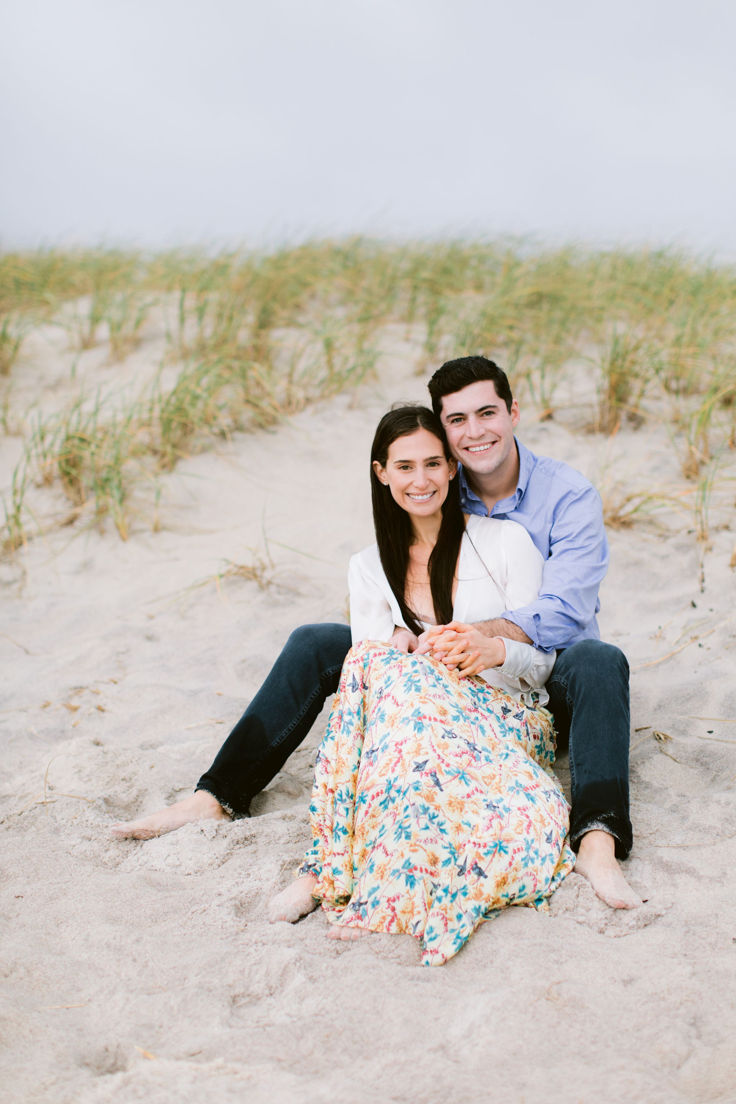 Happy couple sitting together on sandy beach dunes in casual attire.