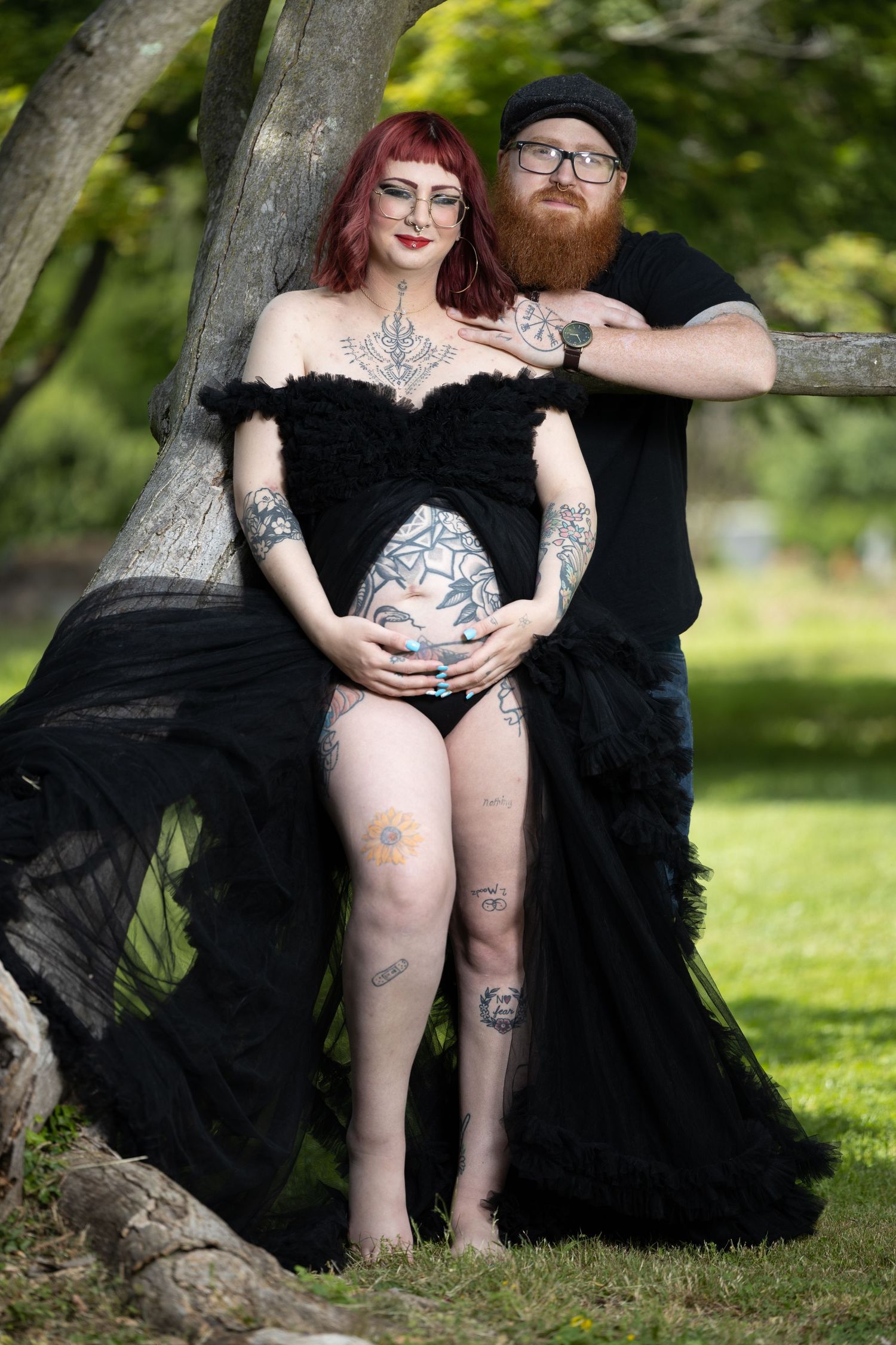 Alternative couple embraces in garden setting with dramatic black flowing dress.