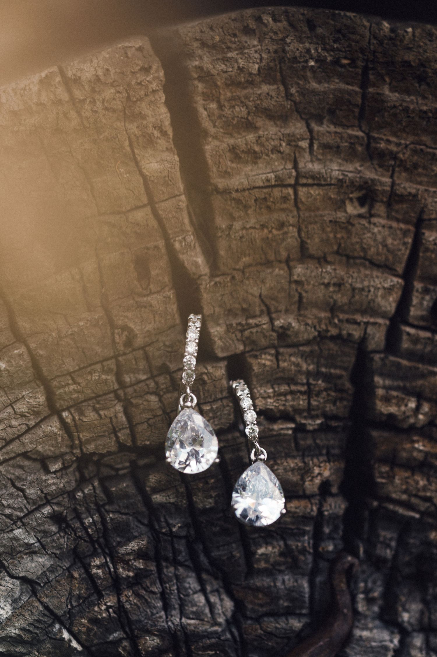 Crystal teardrop earrings photographed against a textured stone surface.