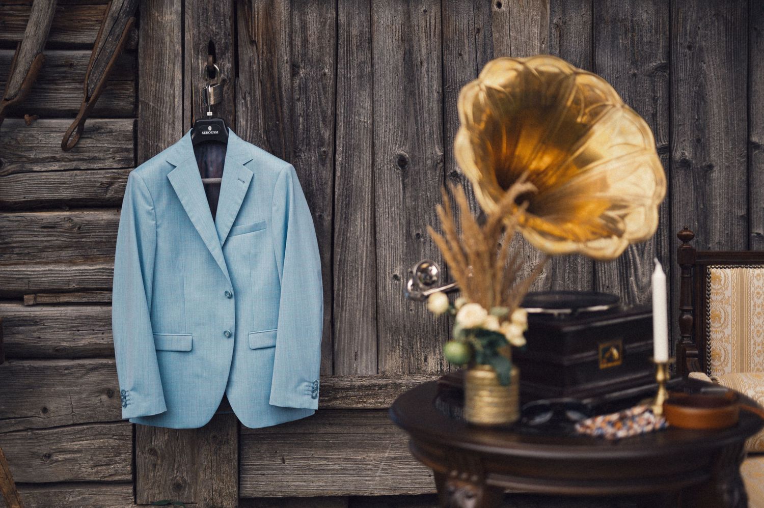 Light blue blazer hangs next to antique gramophone against rustic wooden wall.