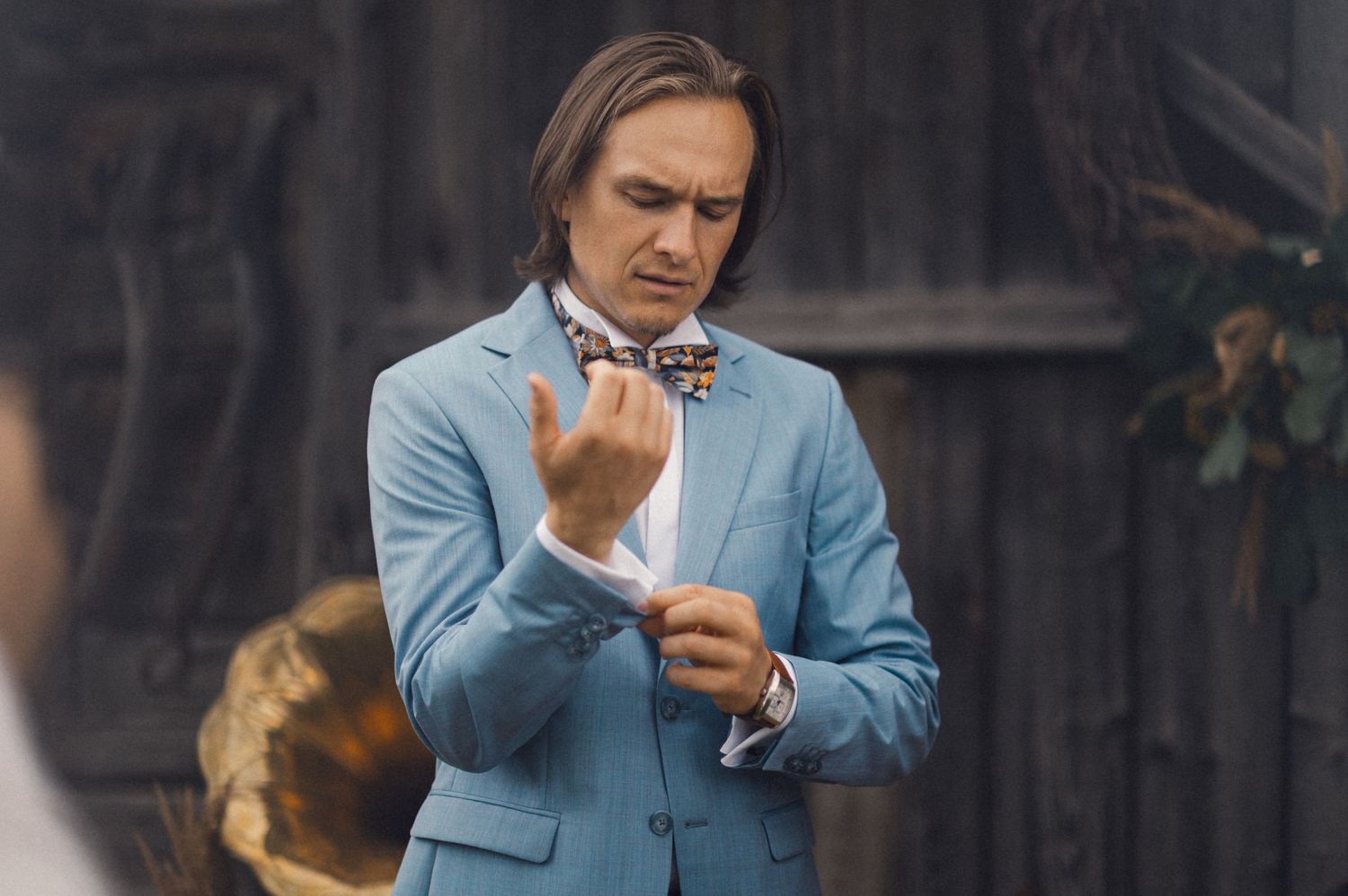 Person in light blue suit adjusting a patterned bowtie outdoors.