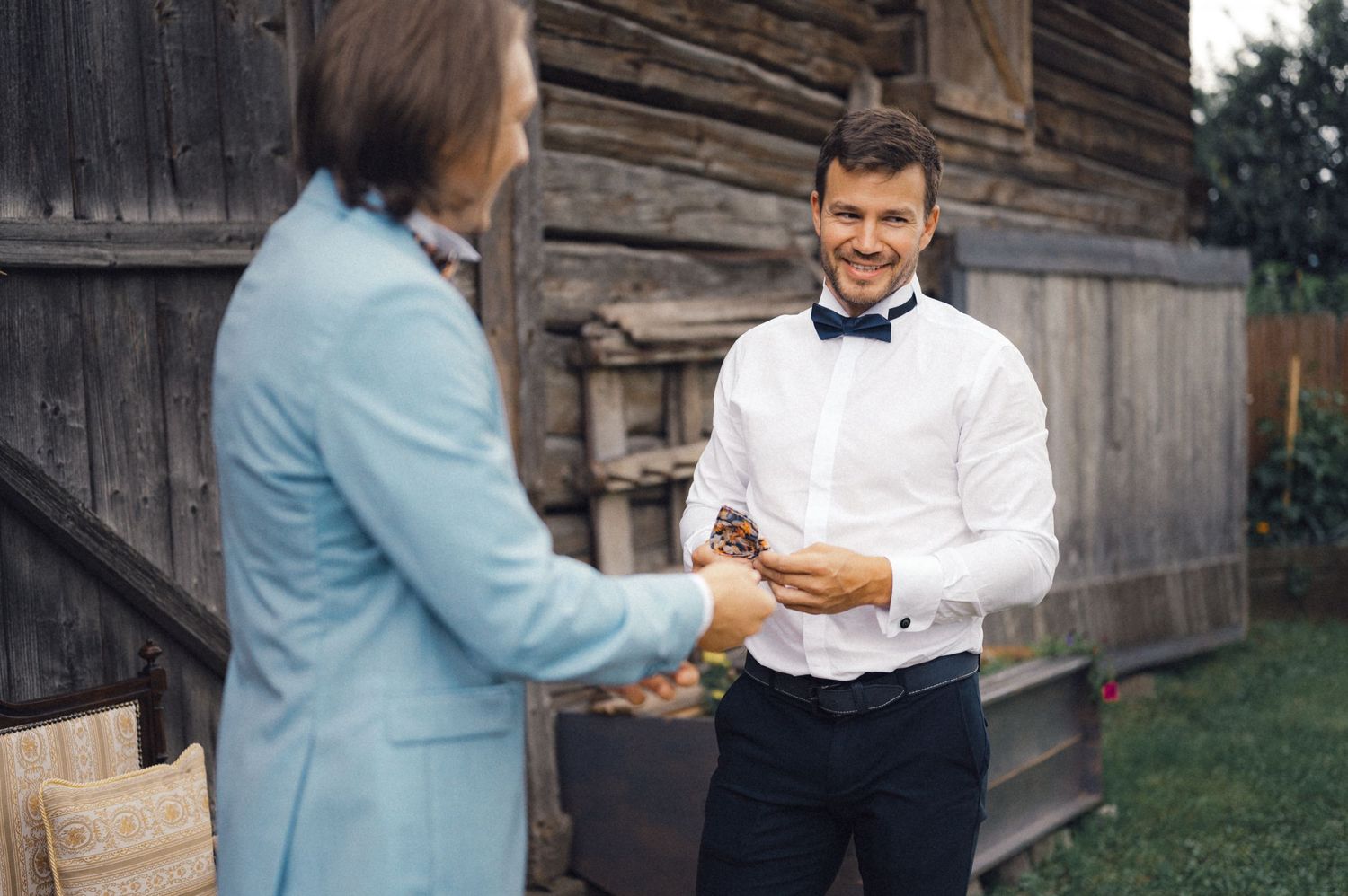 Two people in formal attire having conversation by rustic wooden building.