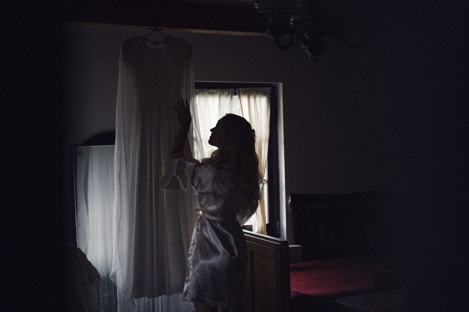 Silhouette of person standing by window in dark moody interior.