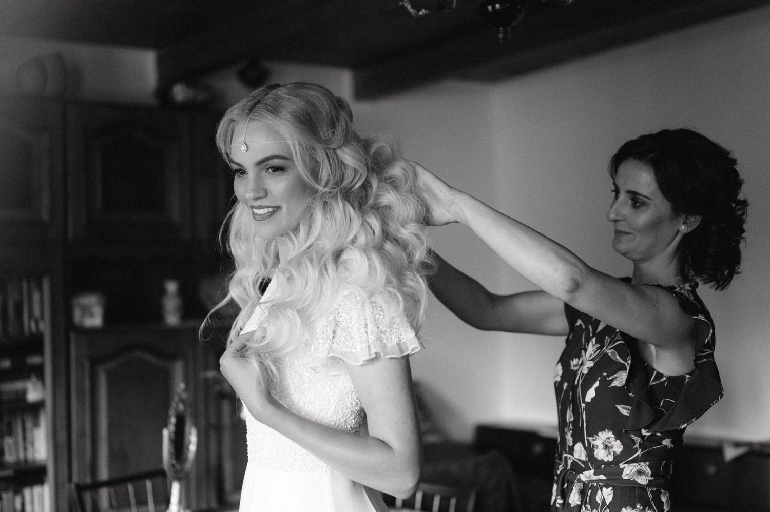 Black and white photo showing bridal preparations with a white lace dress being adjusted.