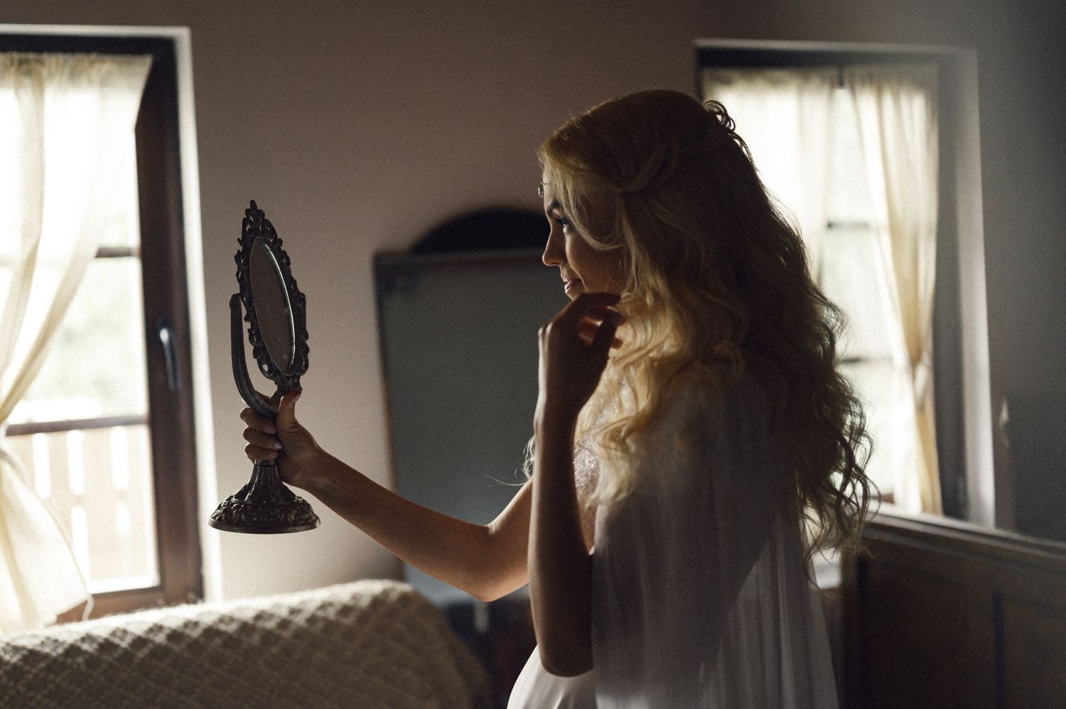 Silhouette by window holding vintage hand mirror in wedding dress.