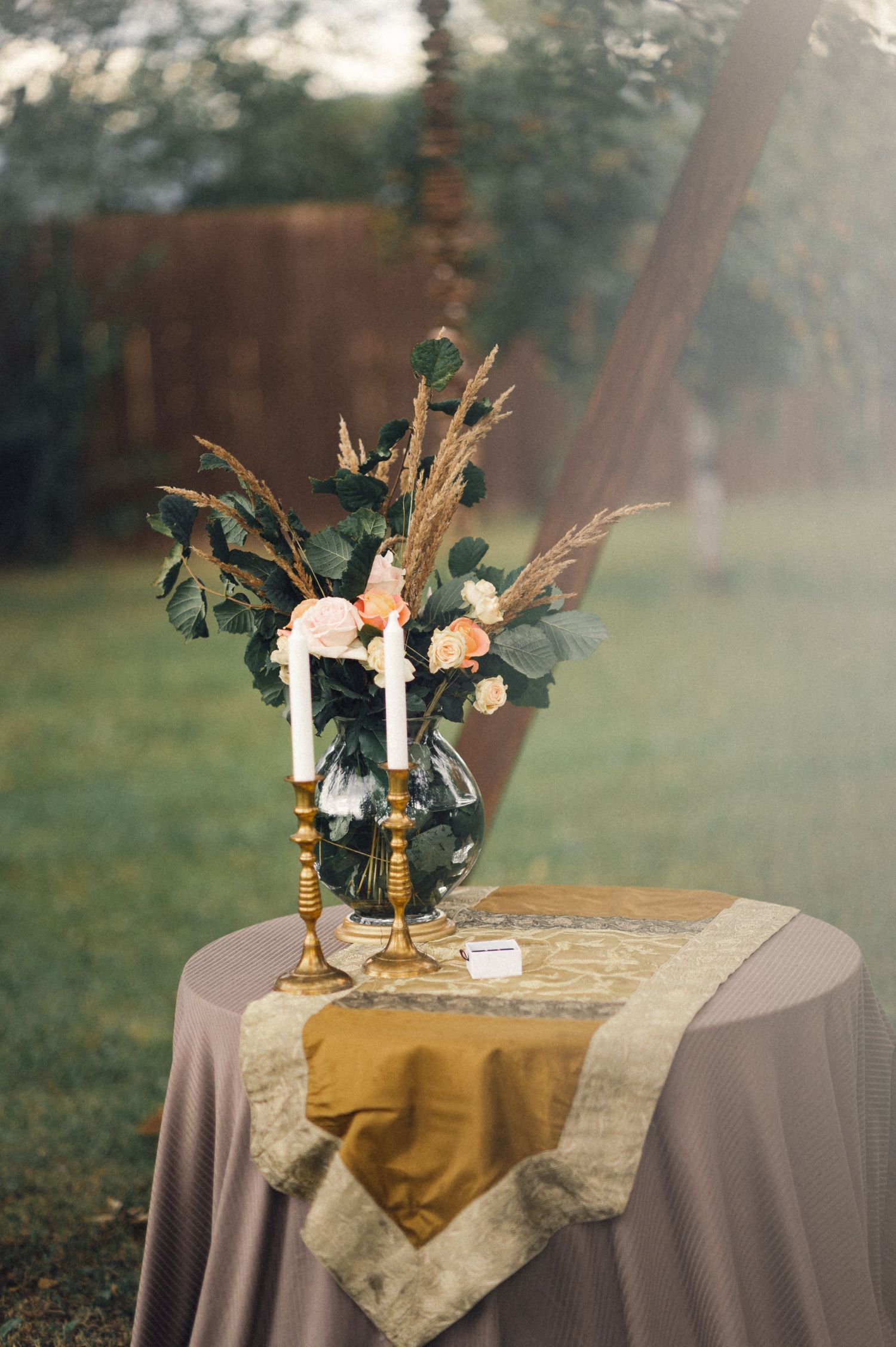 Elegant floral centerpiece with dried grasses and roses on a table with gold and beige linens.
