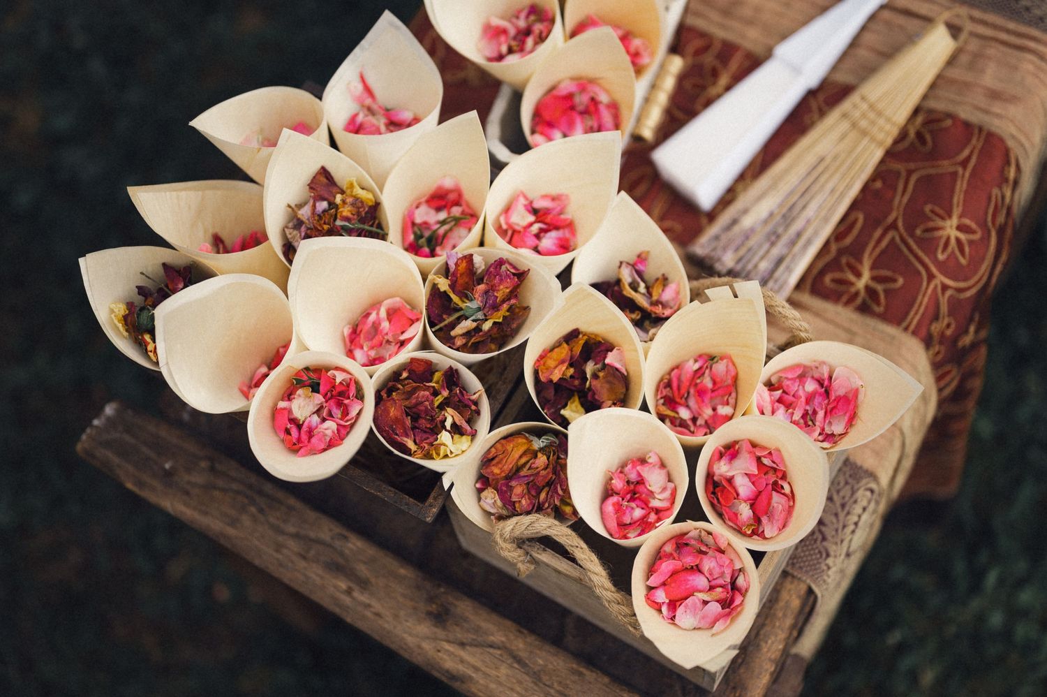 Paper cones filled with colorful flower petals and confetti displayed on wooden surface.