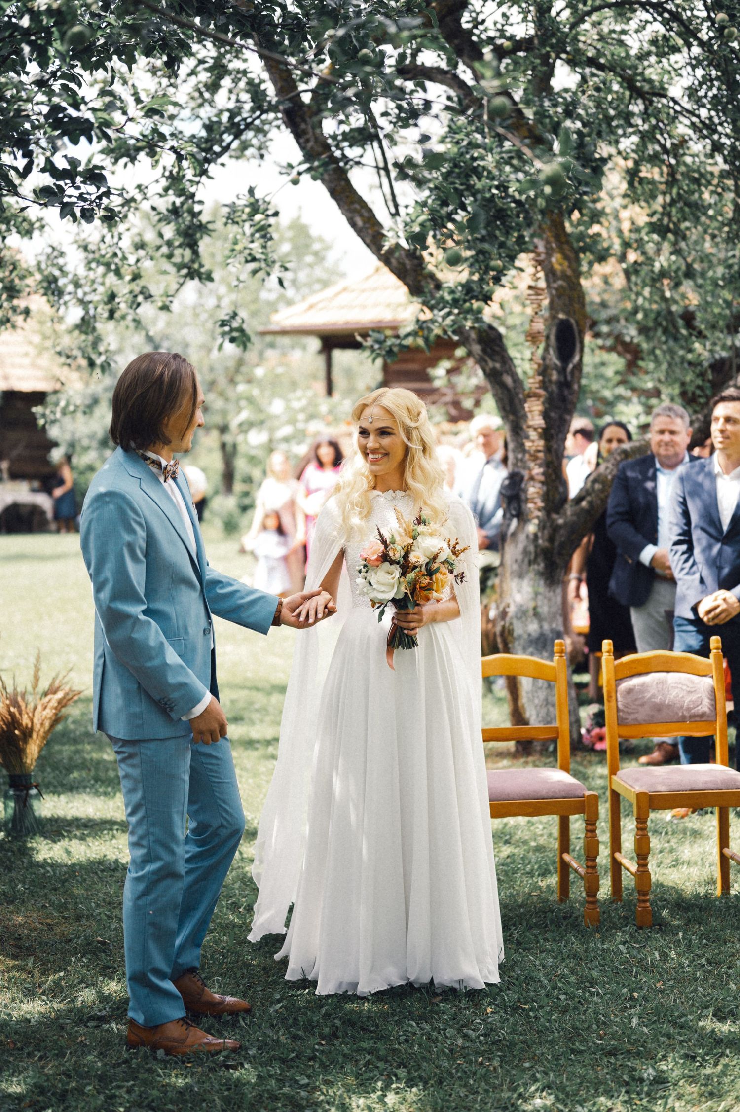 Outdoor garden wedding ceremony with orange chairs and guests watching the couple.