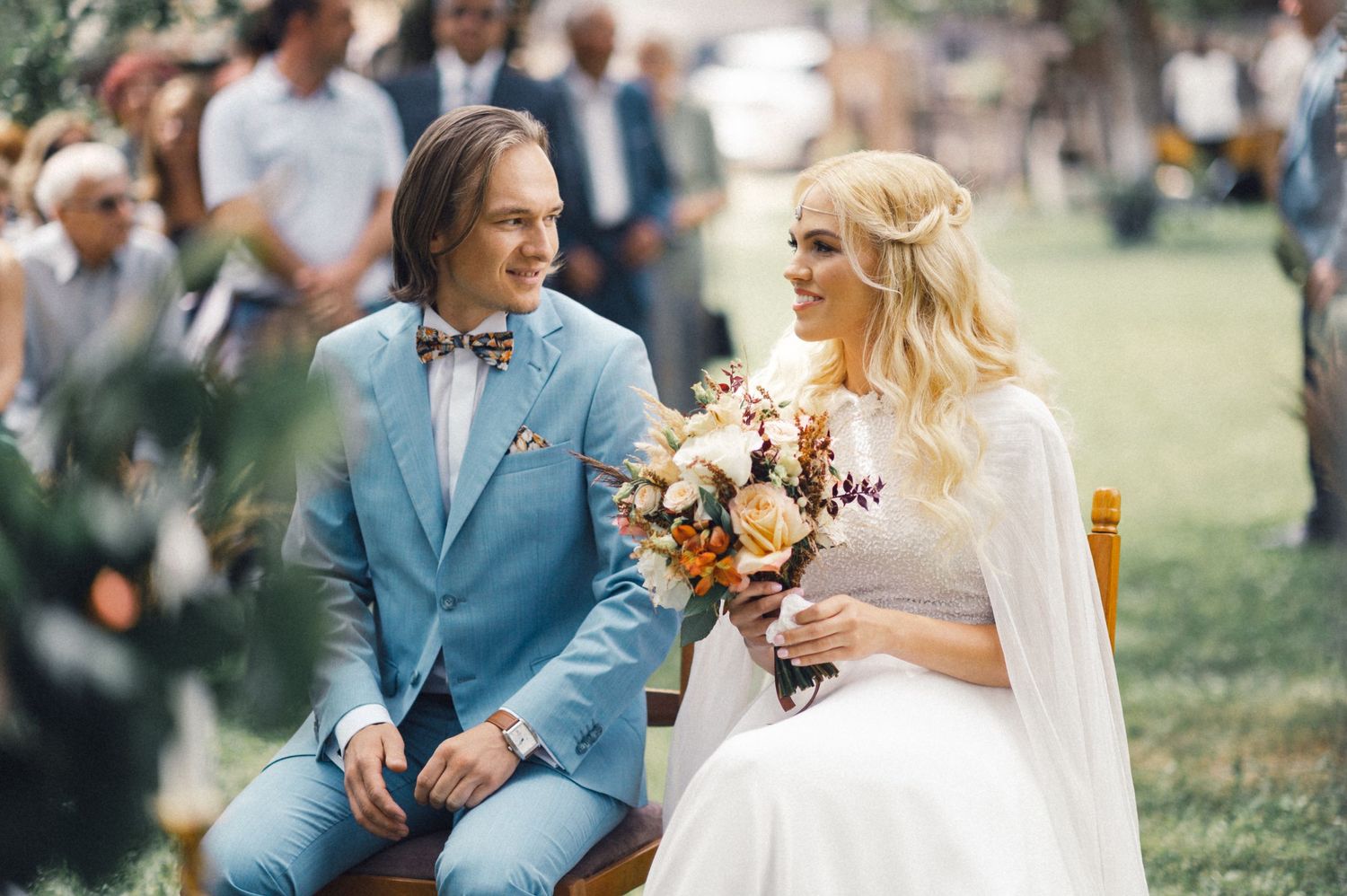 A couple sits together at their garden wedding, with the groom in light blue.