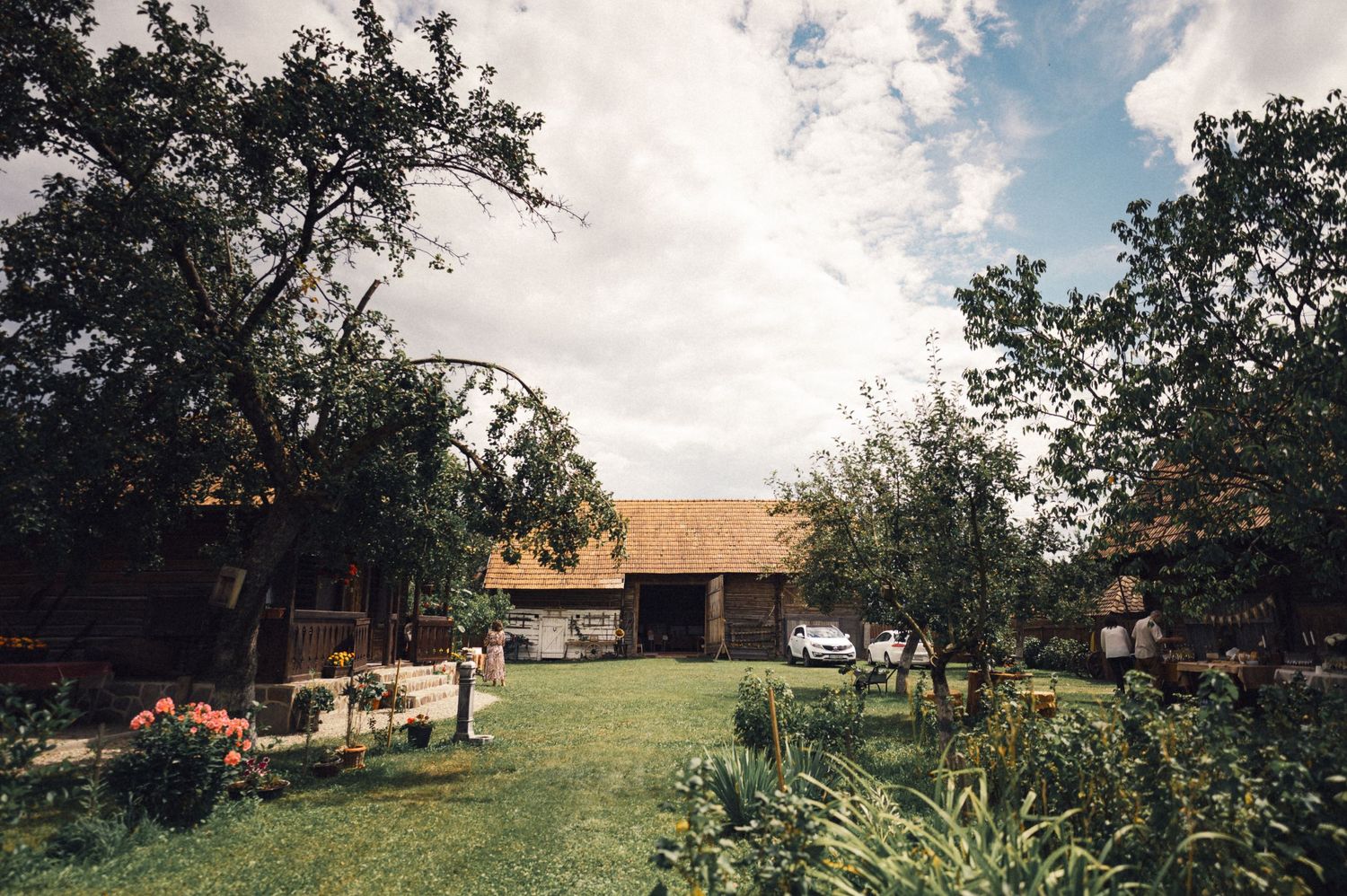 A rustic house with a landscaped garden yard viewed from a distance on a partly cloudy day.