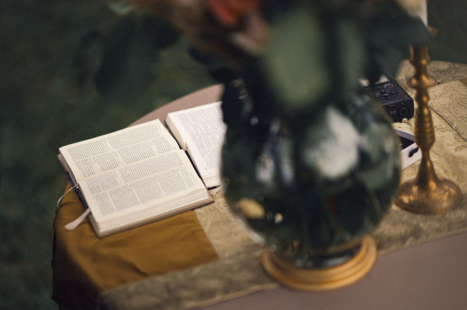 An open book with text lies on a table next to a dark lamp in dim lighting.