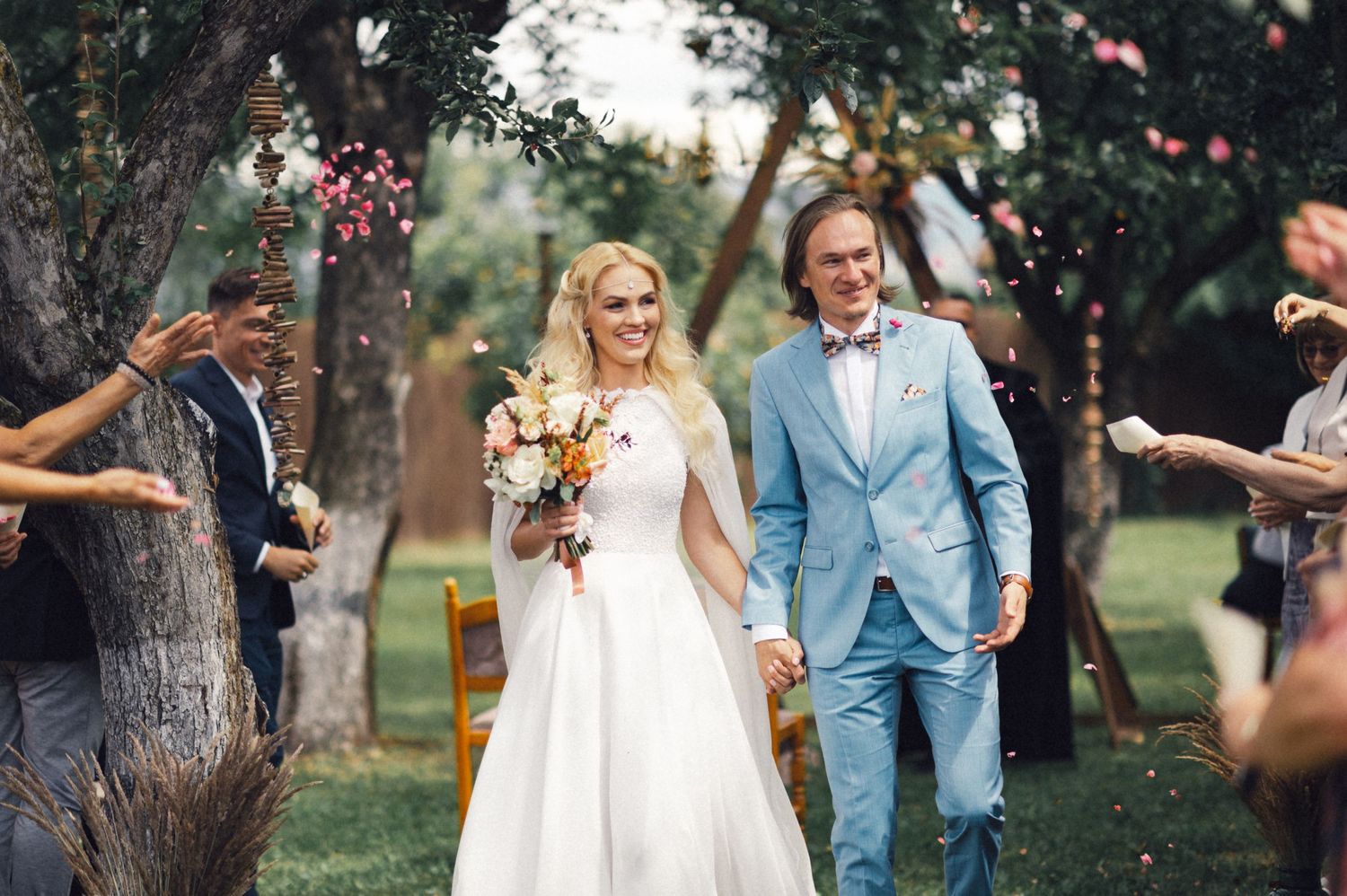 A joyful couple walks down the aisle while guests throw flower petals in celebration.