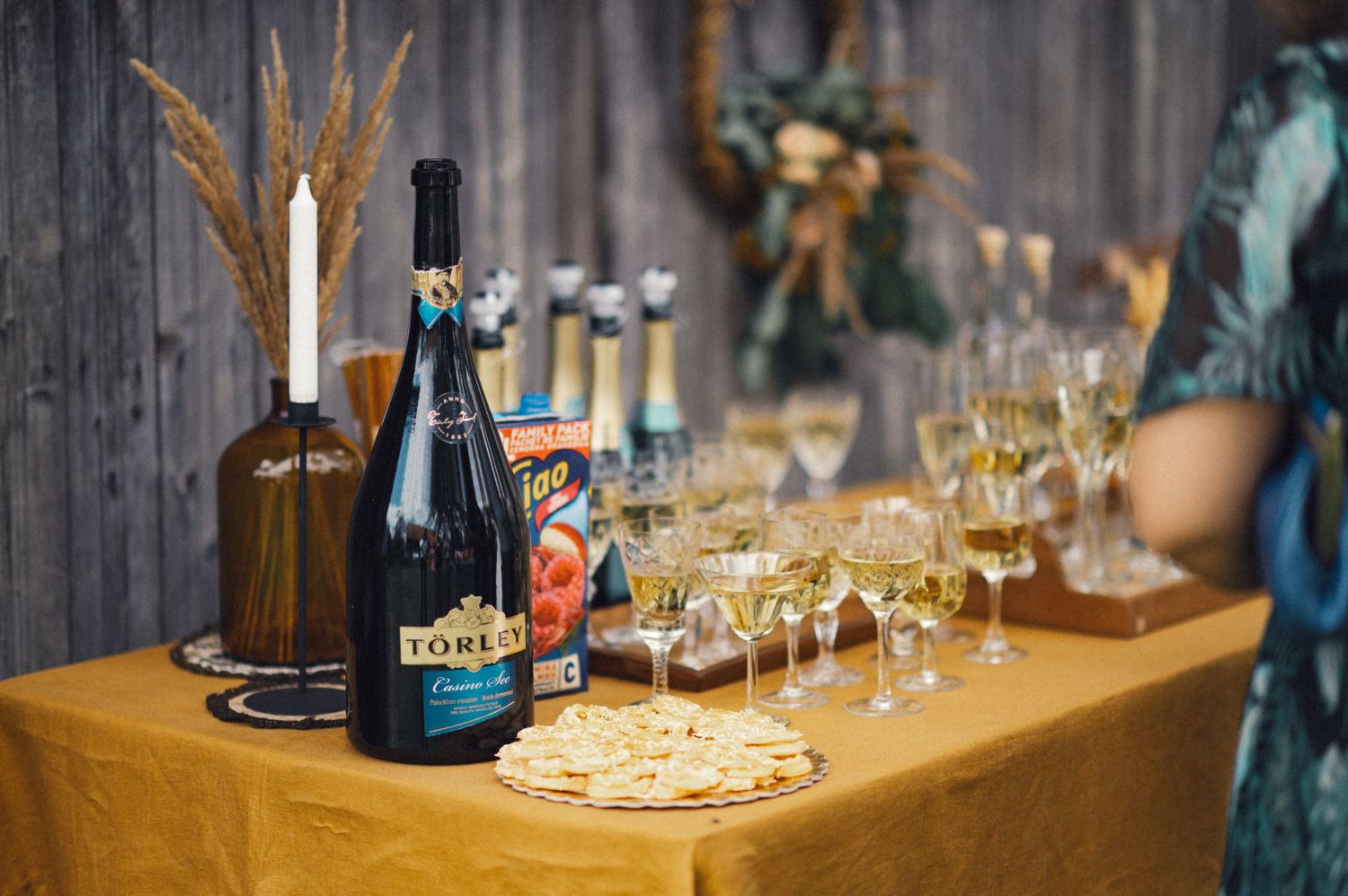 A rustic wedding bar setup with champagne bottles and glasses on an orange tablecloth.