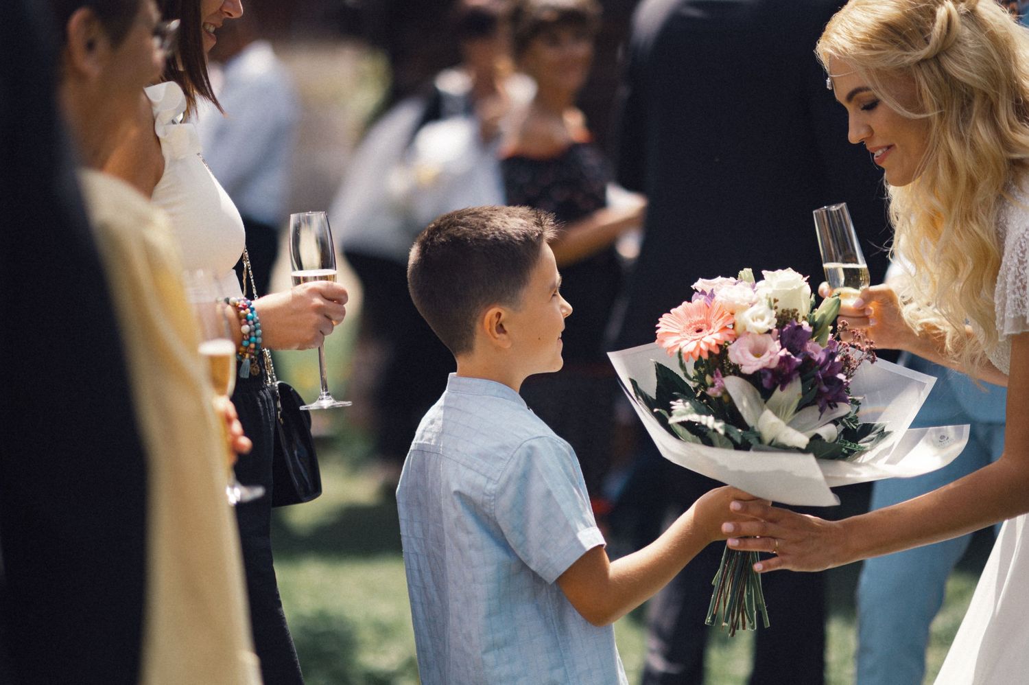 A young boy presents a bouquet of pink flowers at a wedding reception.