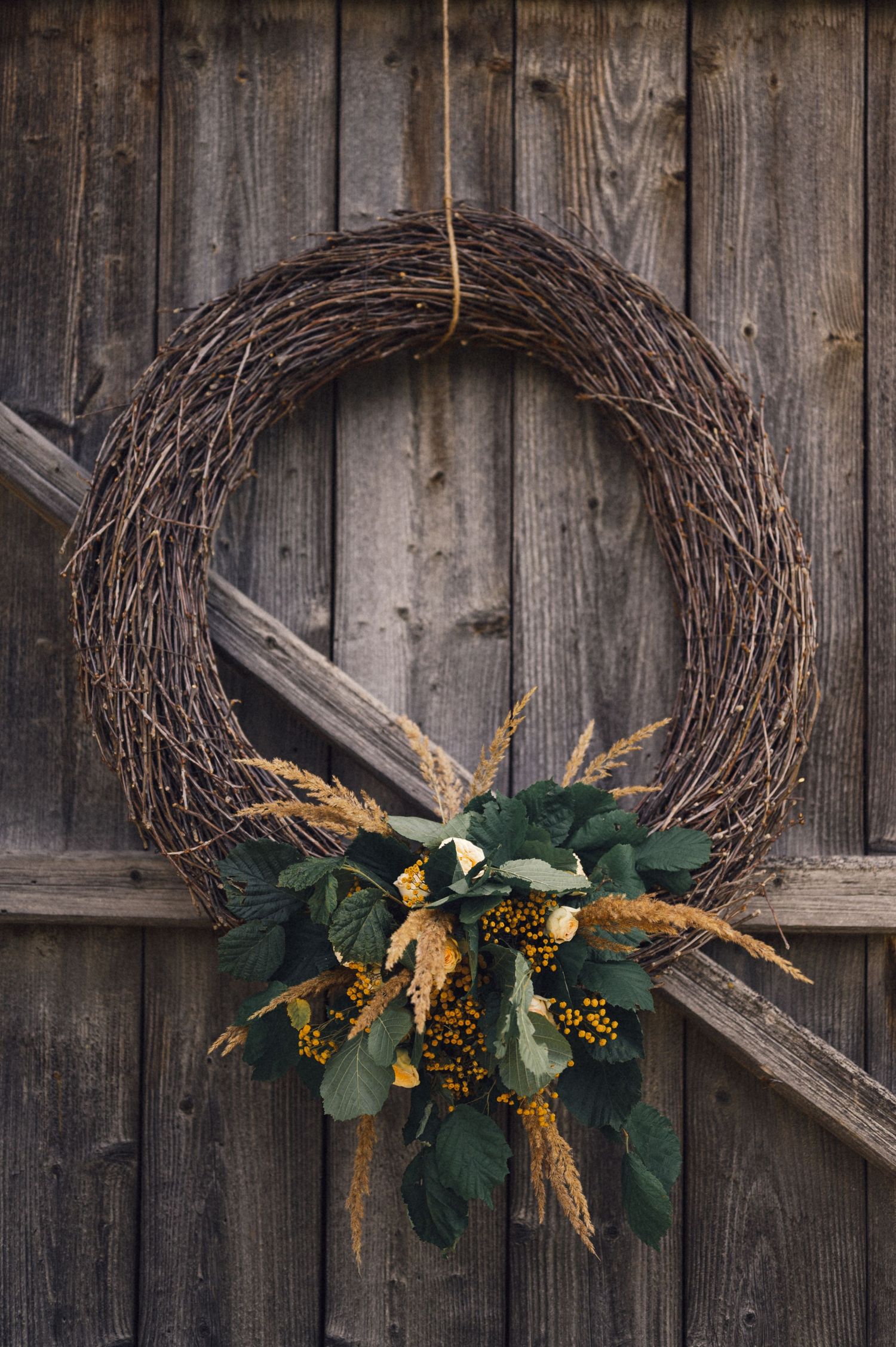 Rustic wreath with green eucalyptus leaves and dried wheat hanging on weathered wooden door.